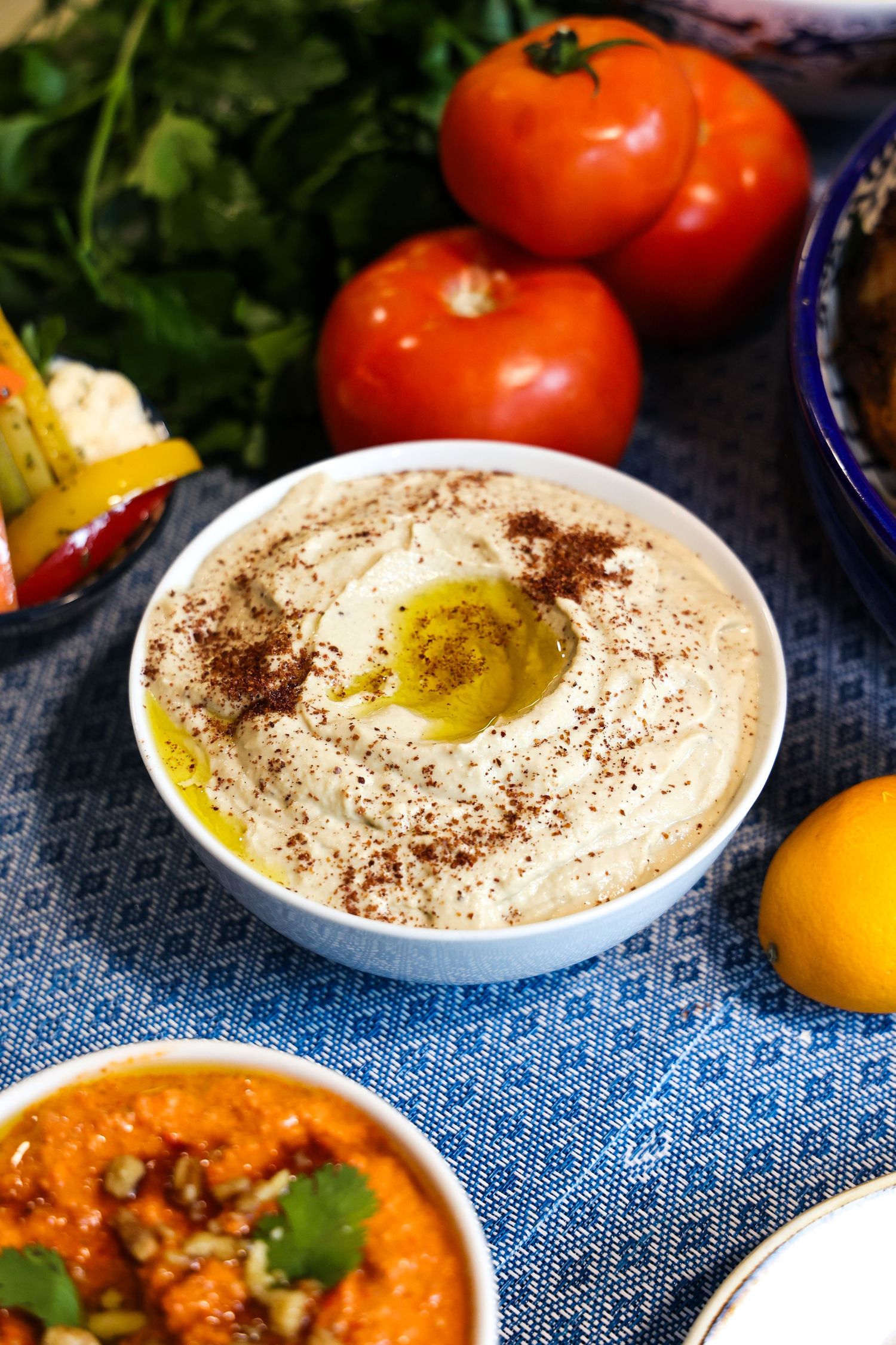 Fresh Mediterranean mezze platter with hummus, tomatoes and garnishes on a blue tablecloth.