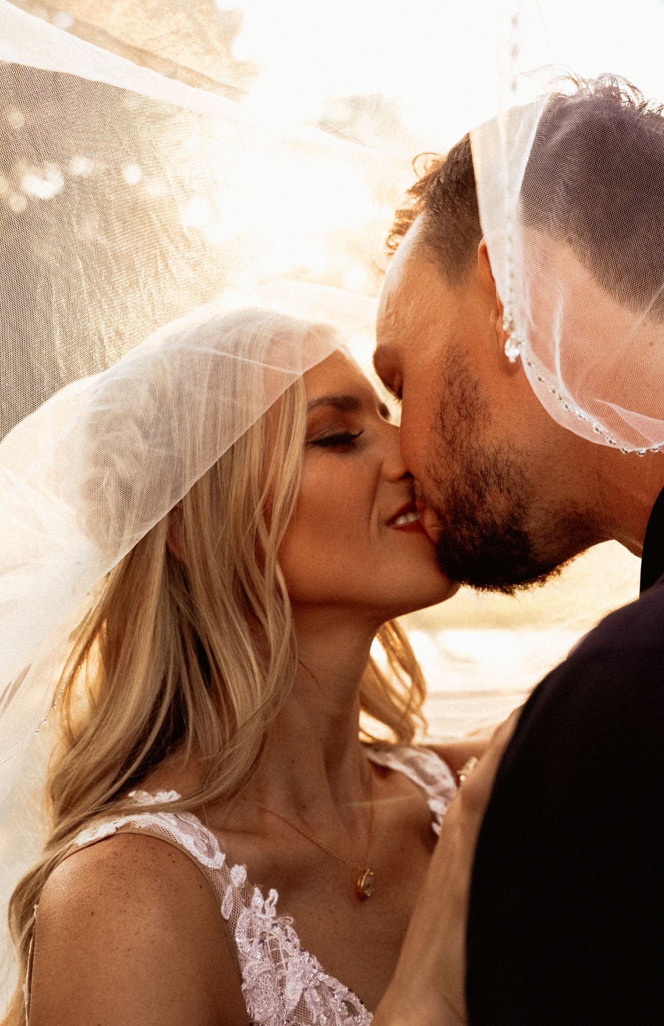 Close-up of wedding couple sharing intimate kiss under flowing veil.
