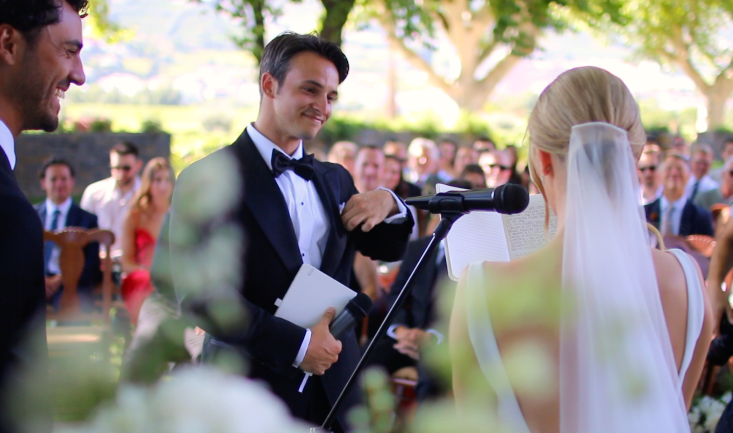 Outdoor garden wedding ceremony with guests watching couple exchange vows.