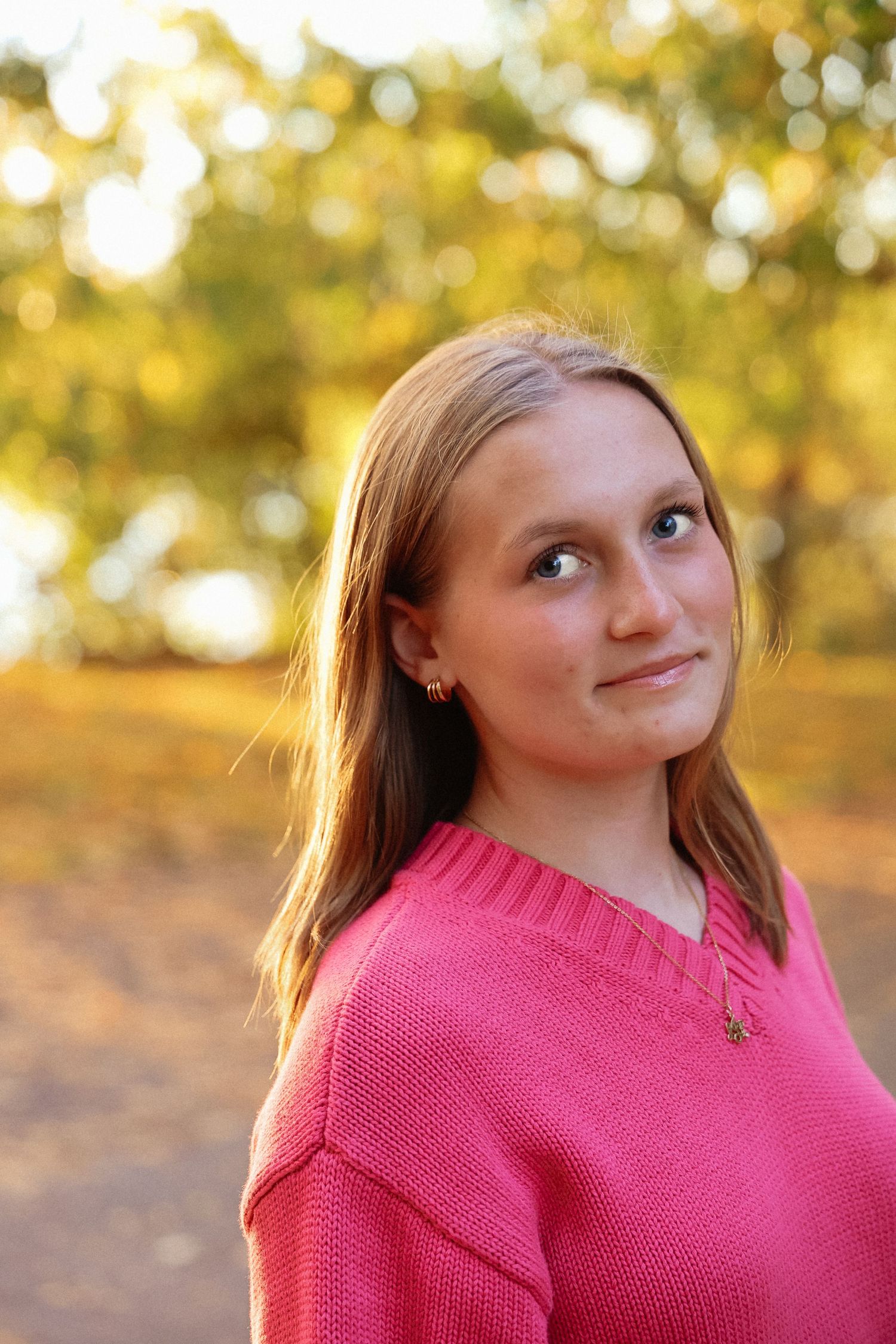 Portrait series in pink sweater with warm autumn bokeh lighting in background.