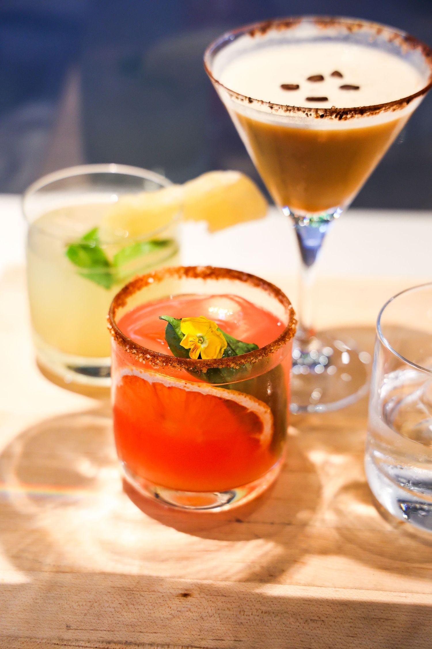 Three elegant cocktails on a wooden surface including an espresso martini and a citrus drink with garnishes.