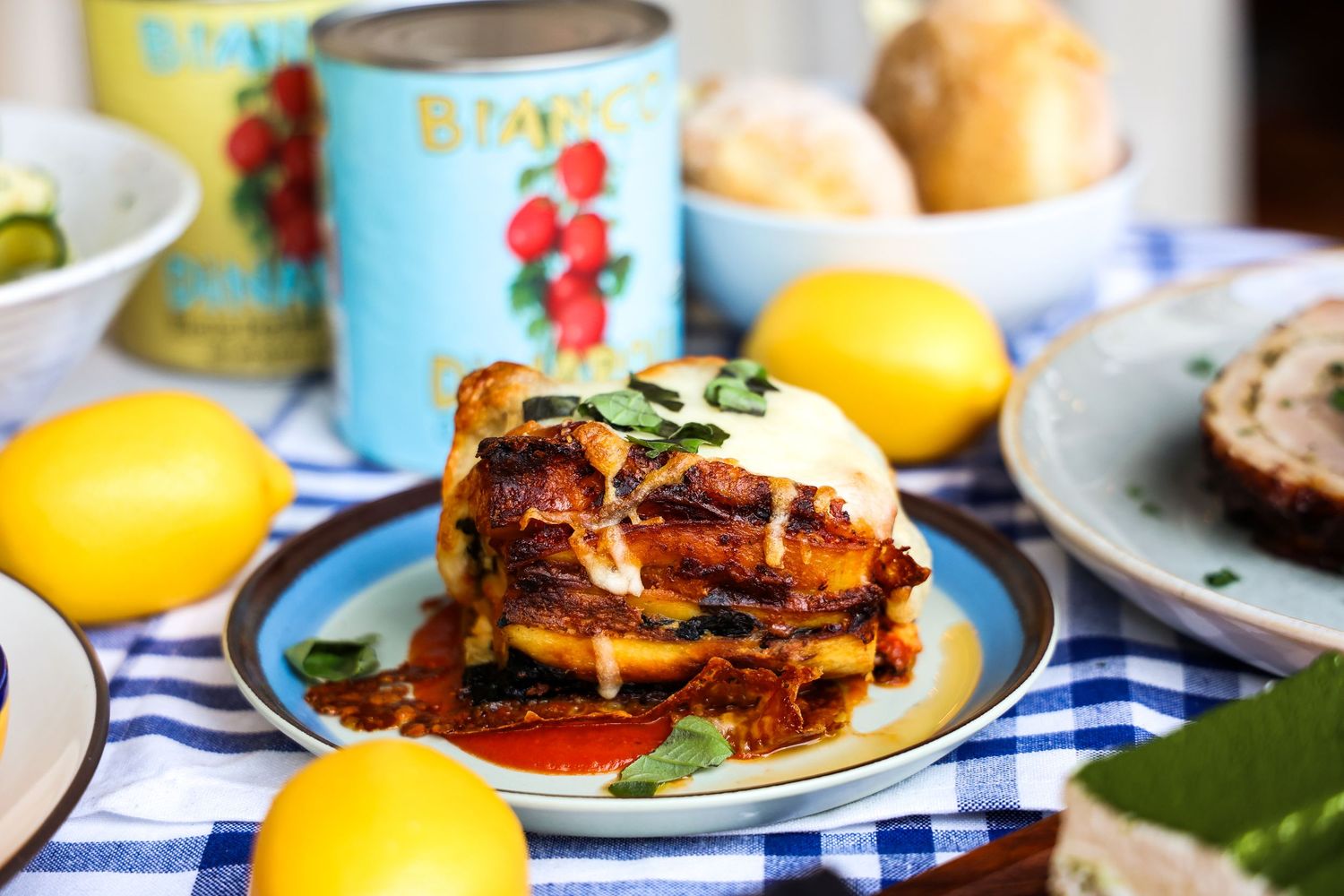 Colorful table setting with burgers and lemons on blue checkered tablecloth.