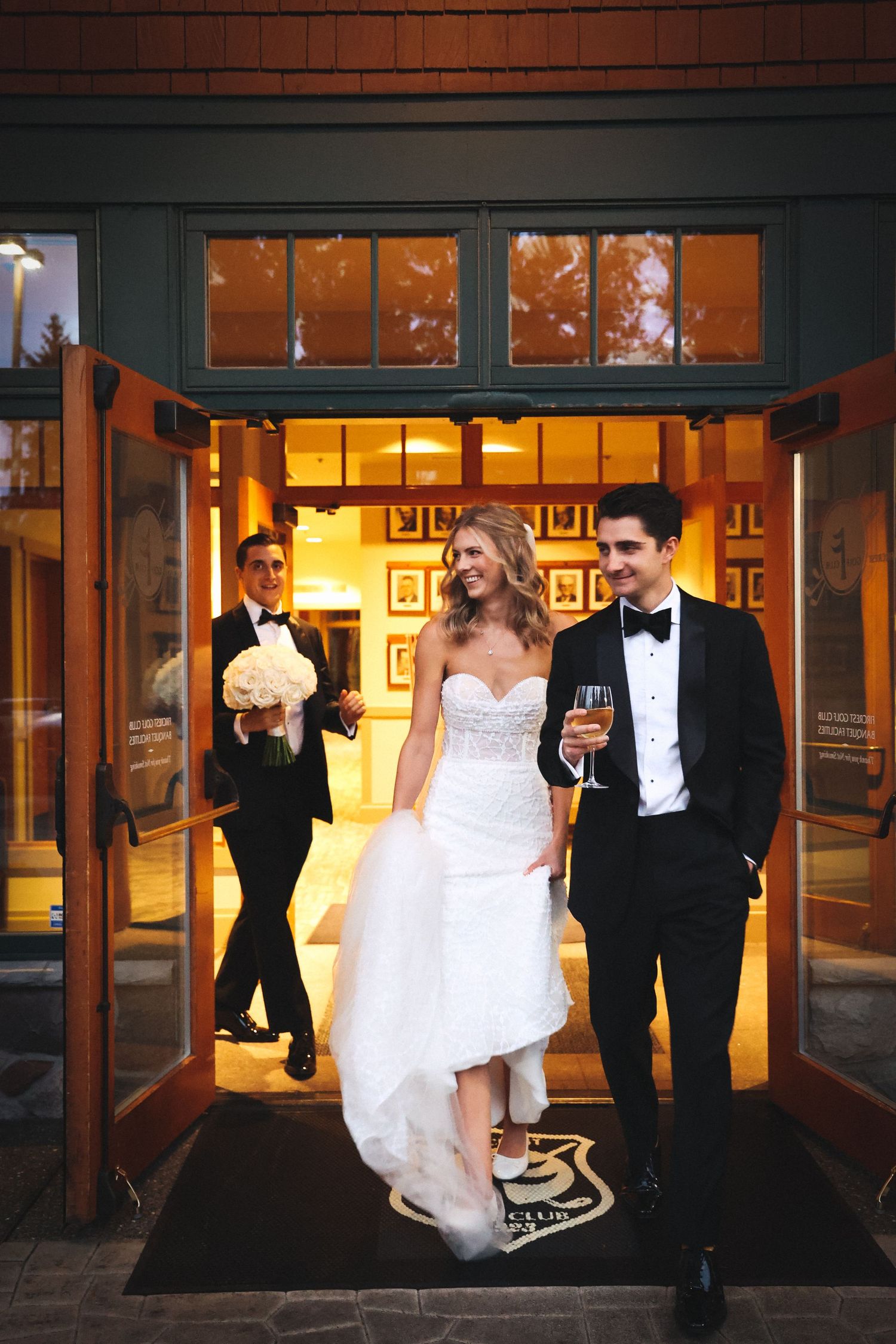 Wedding couple exiting venue at night through illuminated doorway.