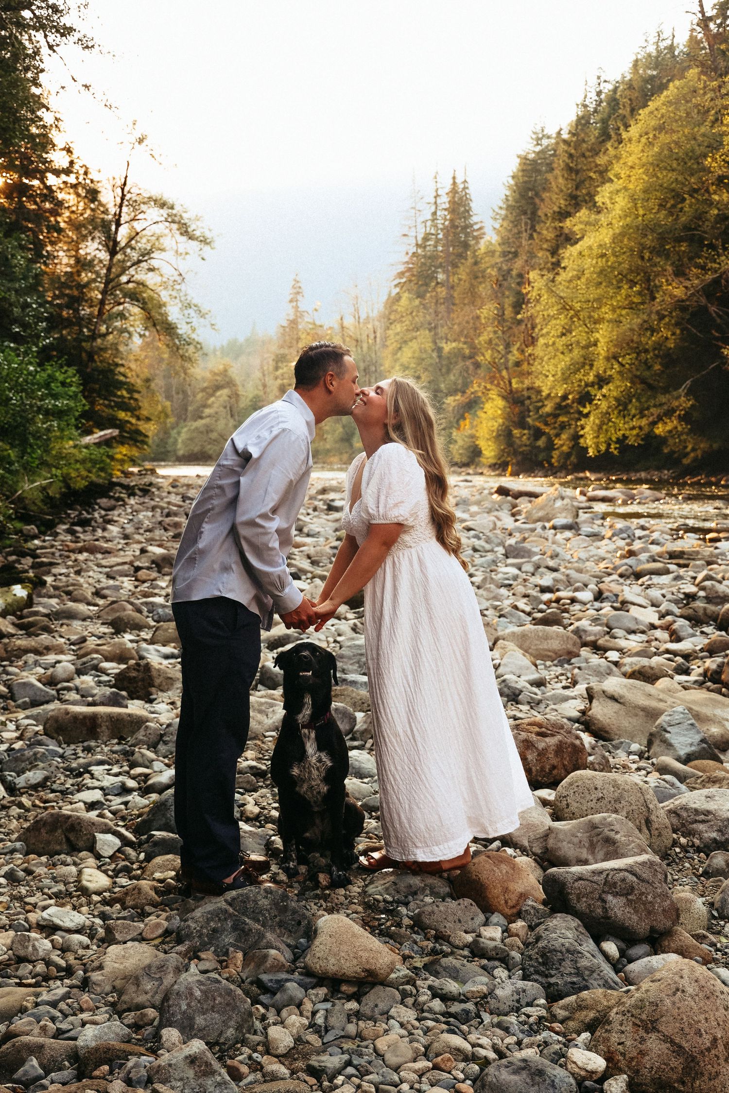 Couple shares romantic moments on rocky riverbed surrounded by autumn forest.