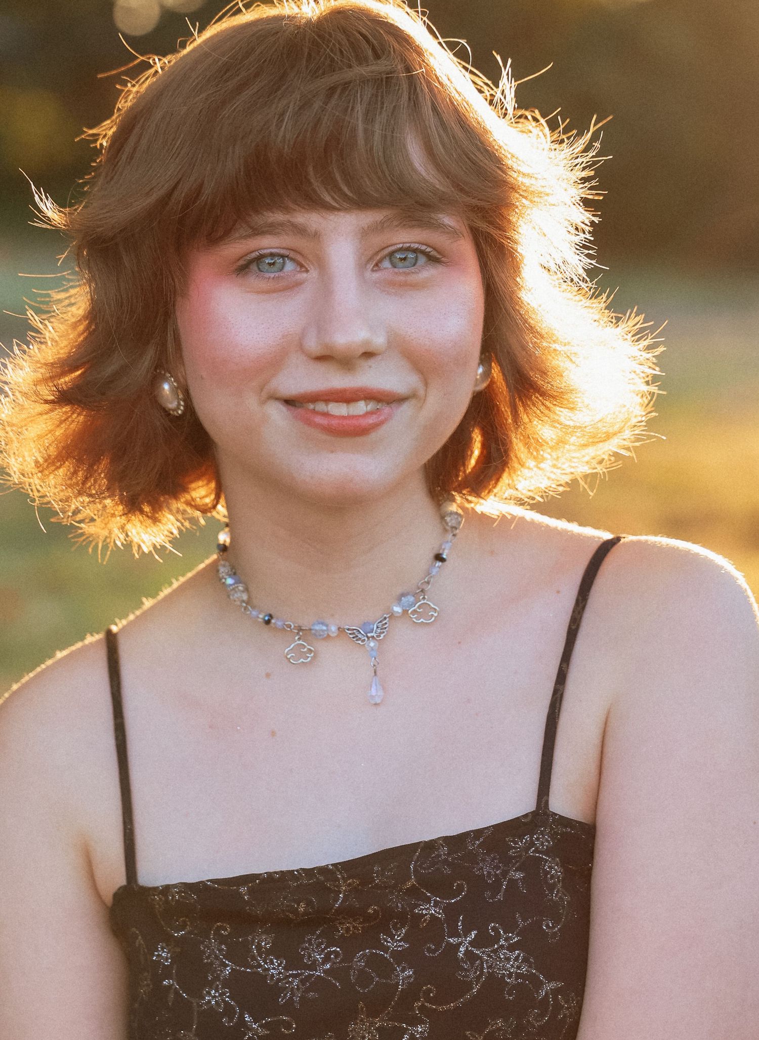 Portrait of person with short hair backlit by golden sunset wearing sparkly jewelry.