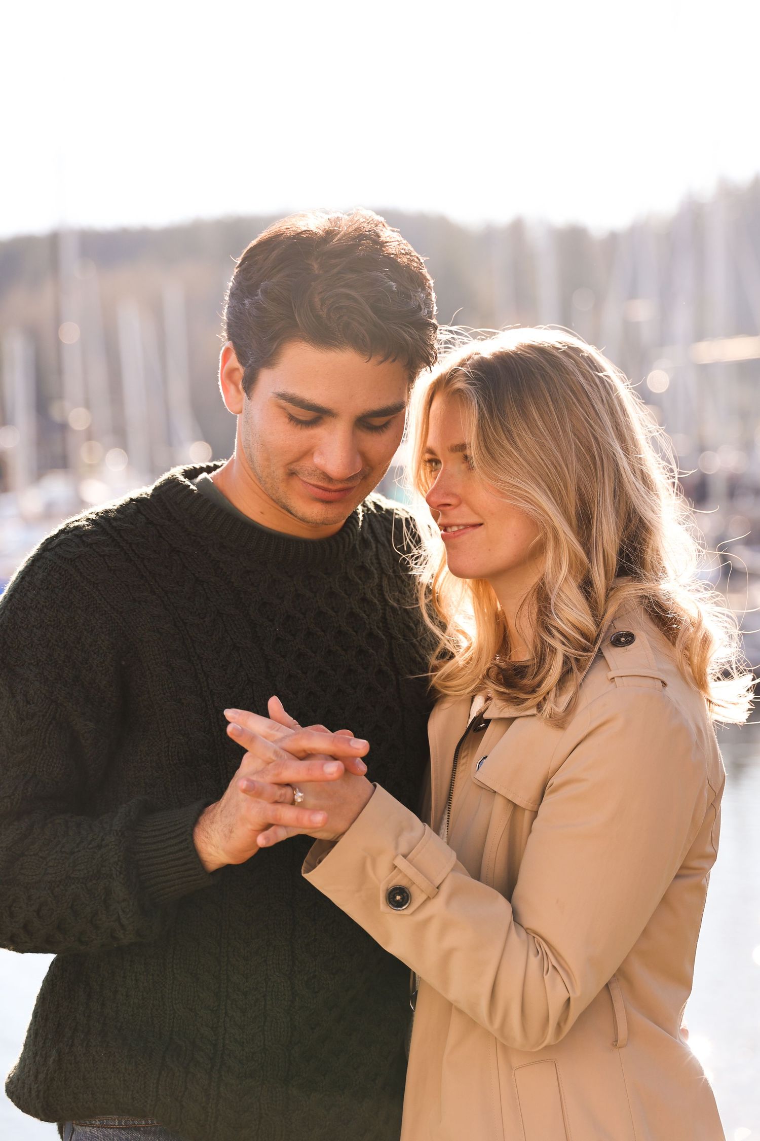 A couple shares a tender moment by a marina on a bright day.