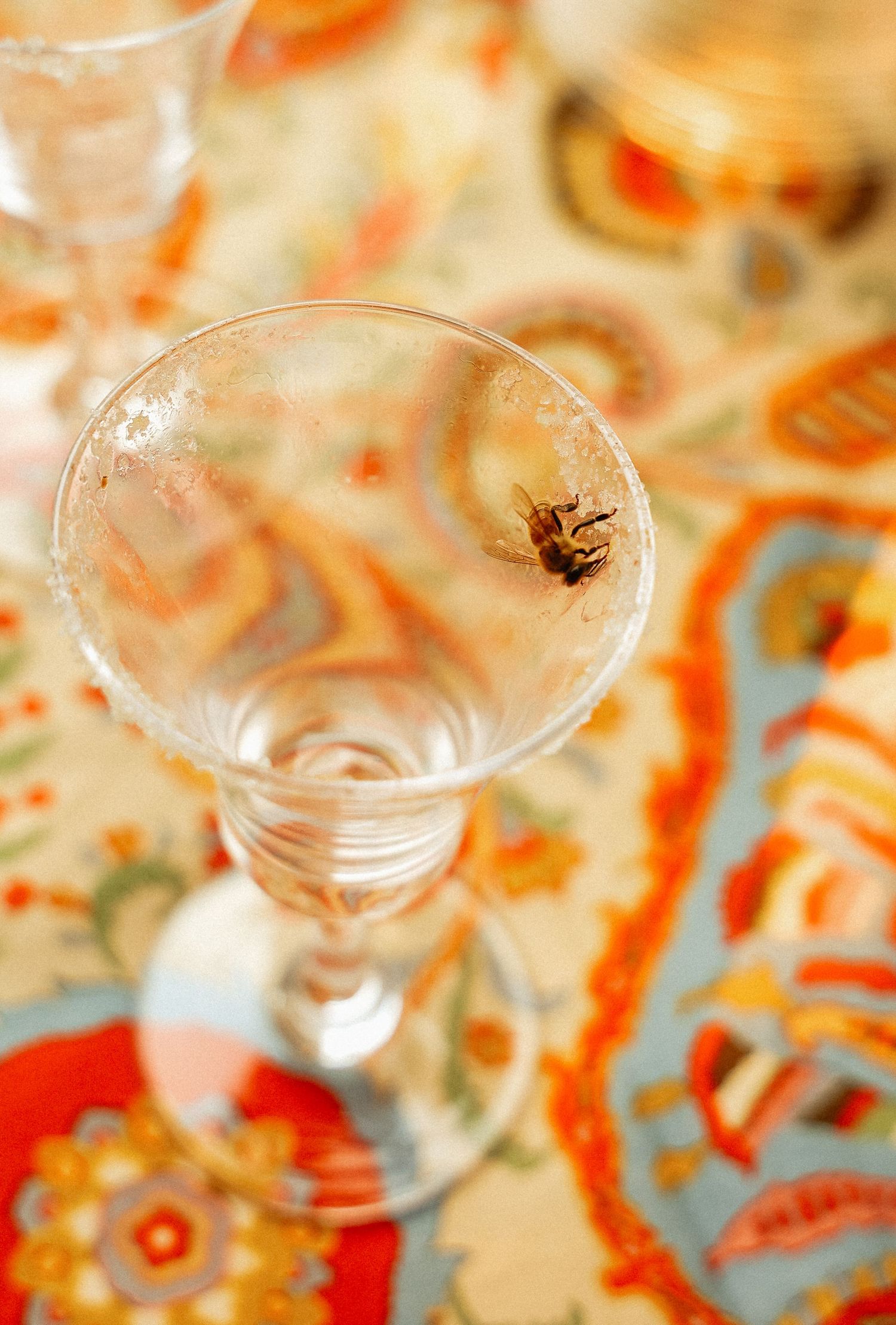 A decorative martini glass sits empty on a table with blurred orange and red patterns in the background.