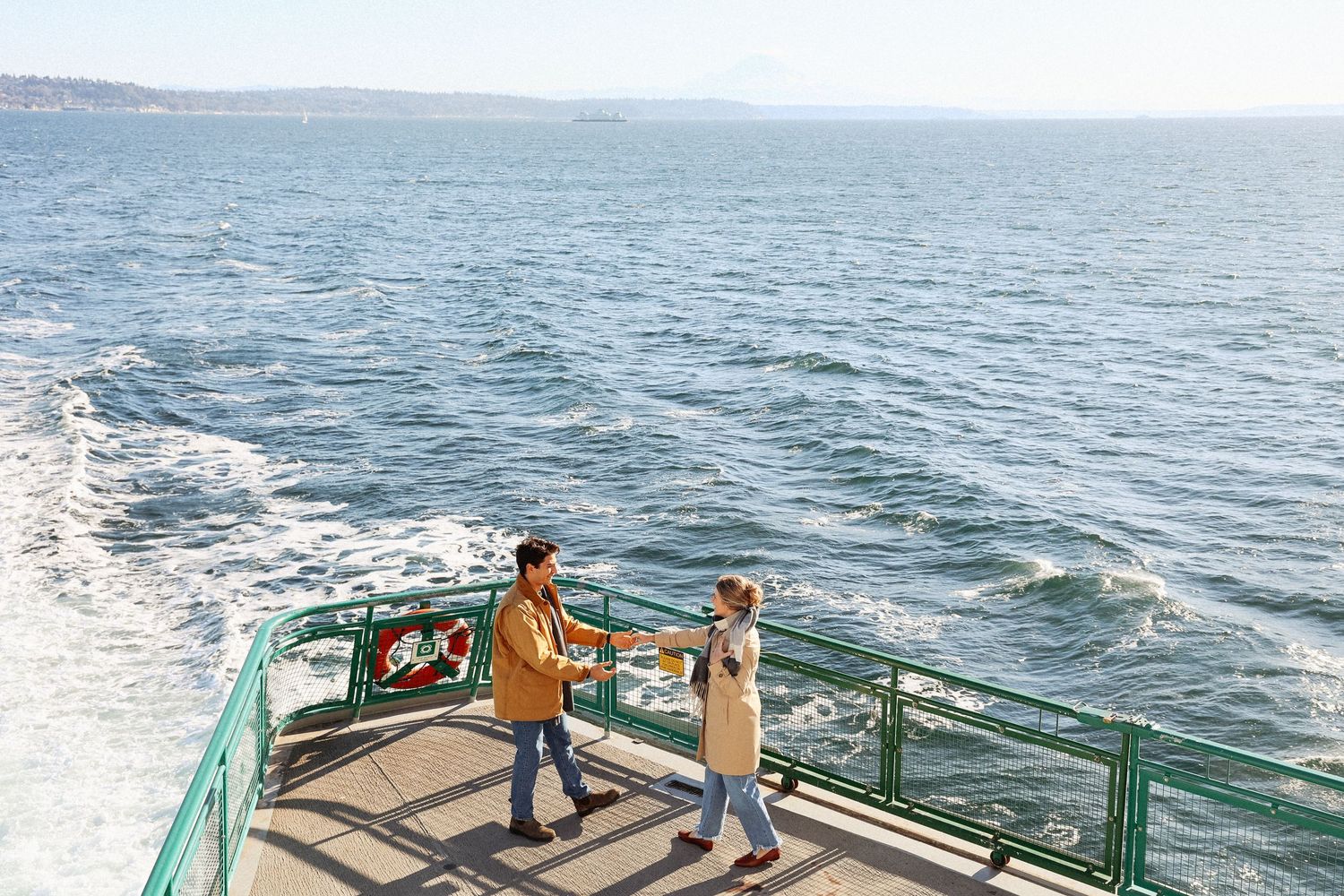 A couple enjoys a romantic moment on a ferry deck overlooking the ocean.