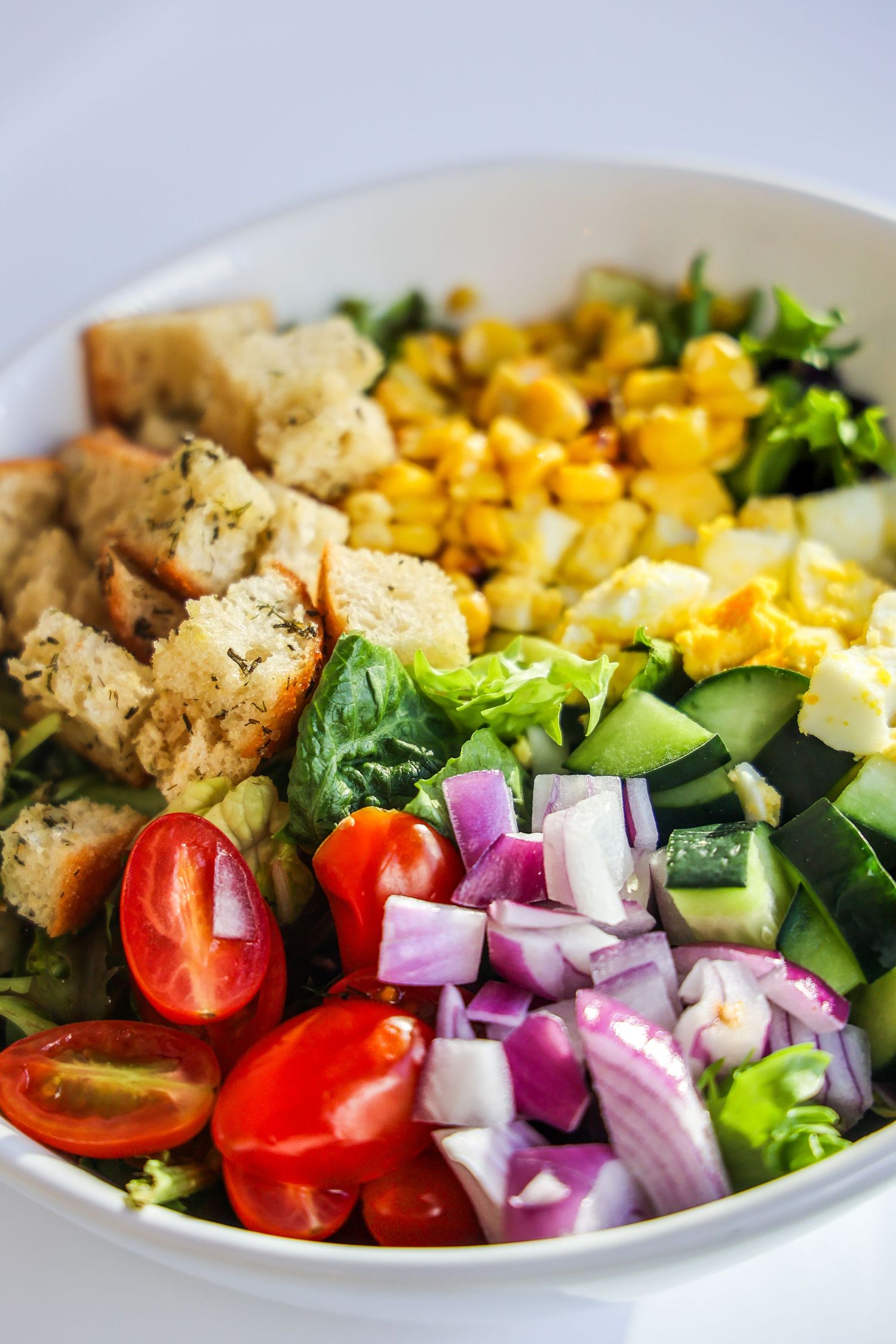 Fresh garden salad with colorful vegetables, corn, and croutons arranged in a white bowl.