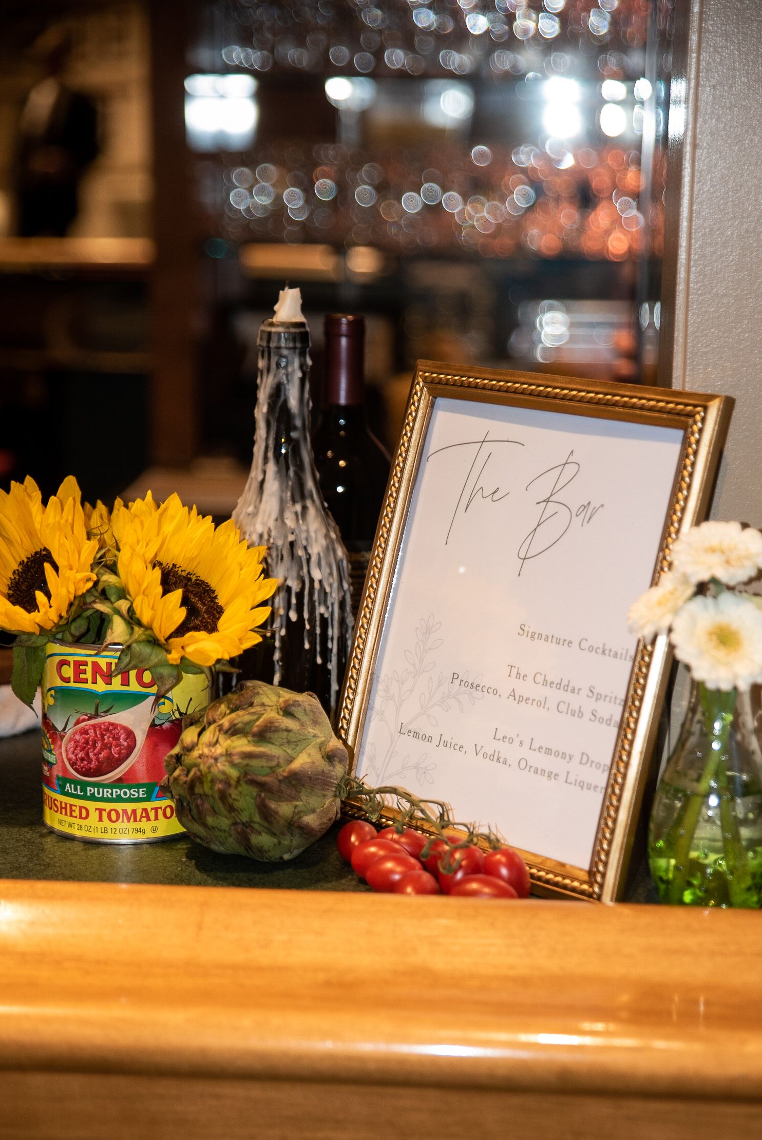 Bar menu display with sunflowers, tomatoes and decorative frame on wooden counter.