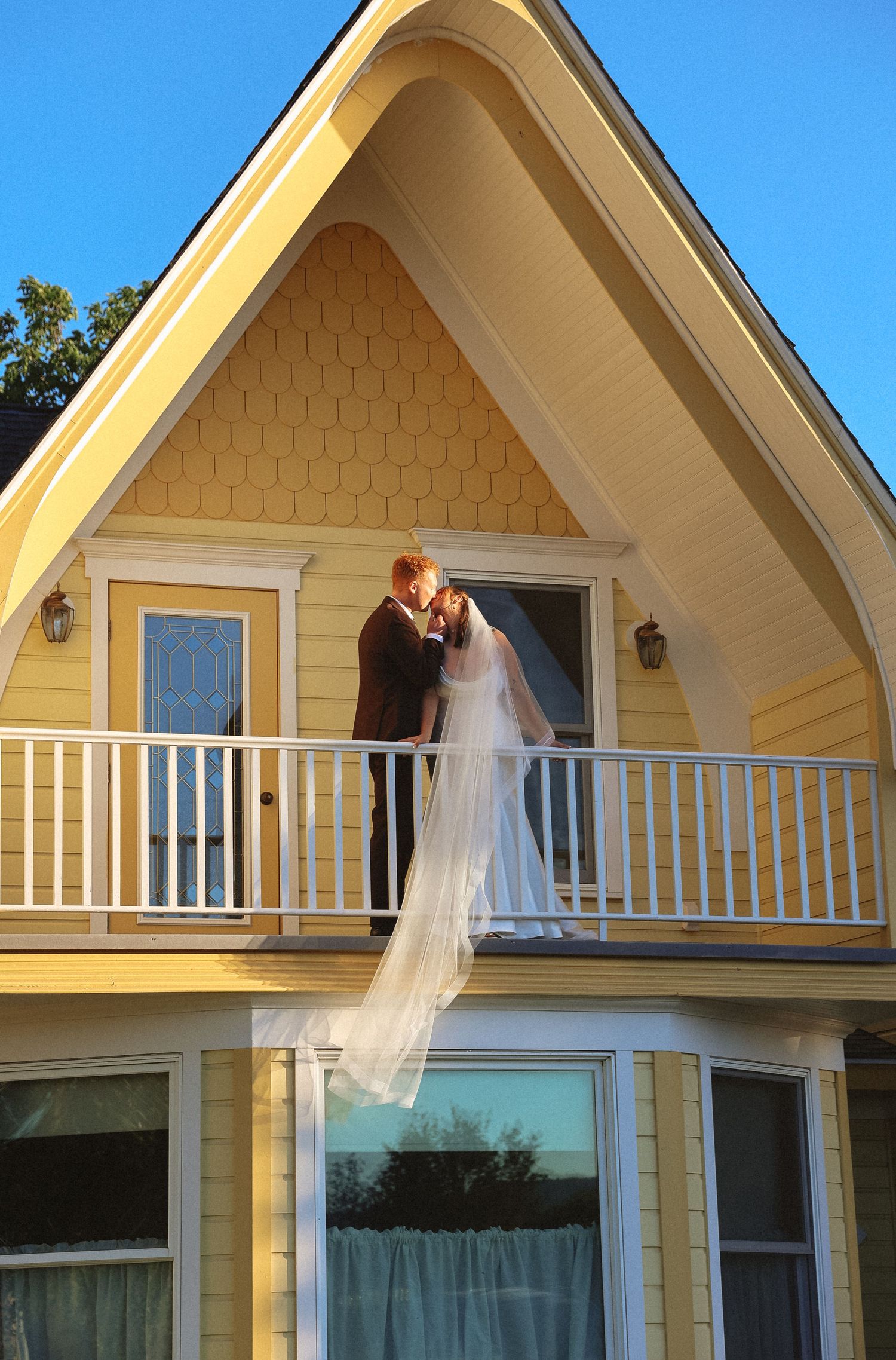 Yellow A-frame house exterior showcasing wedding dress on second floor balcony.