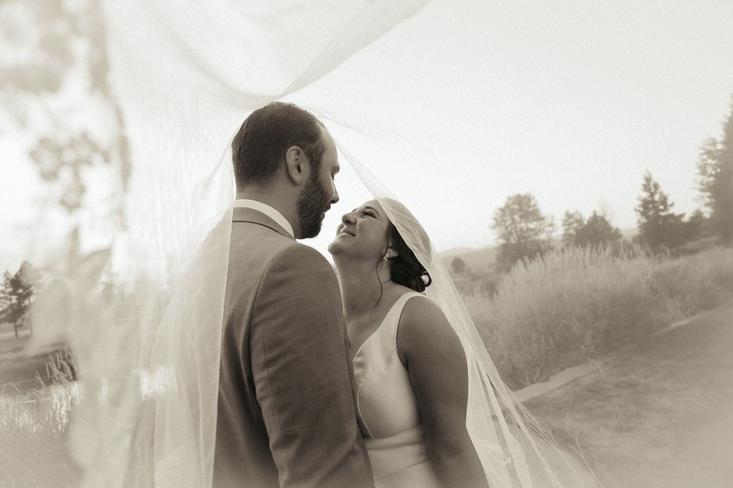 A romantic couple embraces on a misty path in a dreamy black and white outdoor setting.