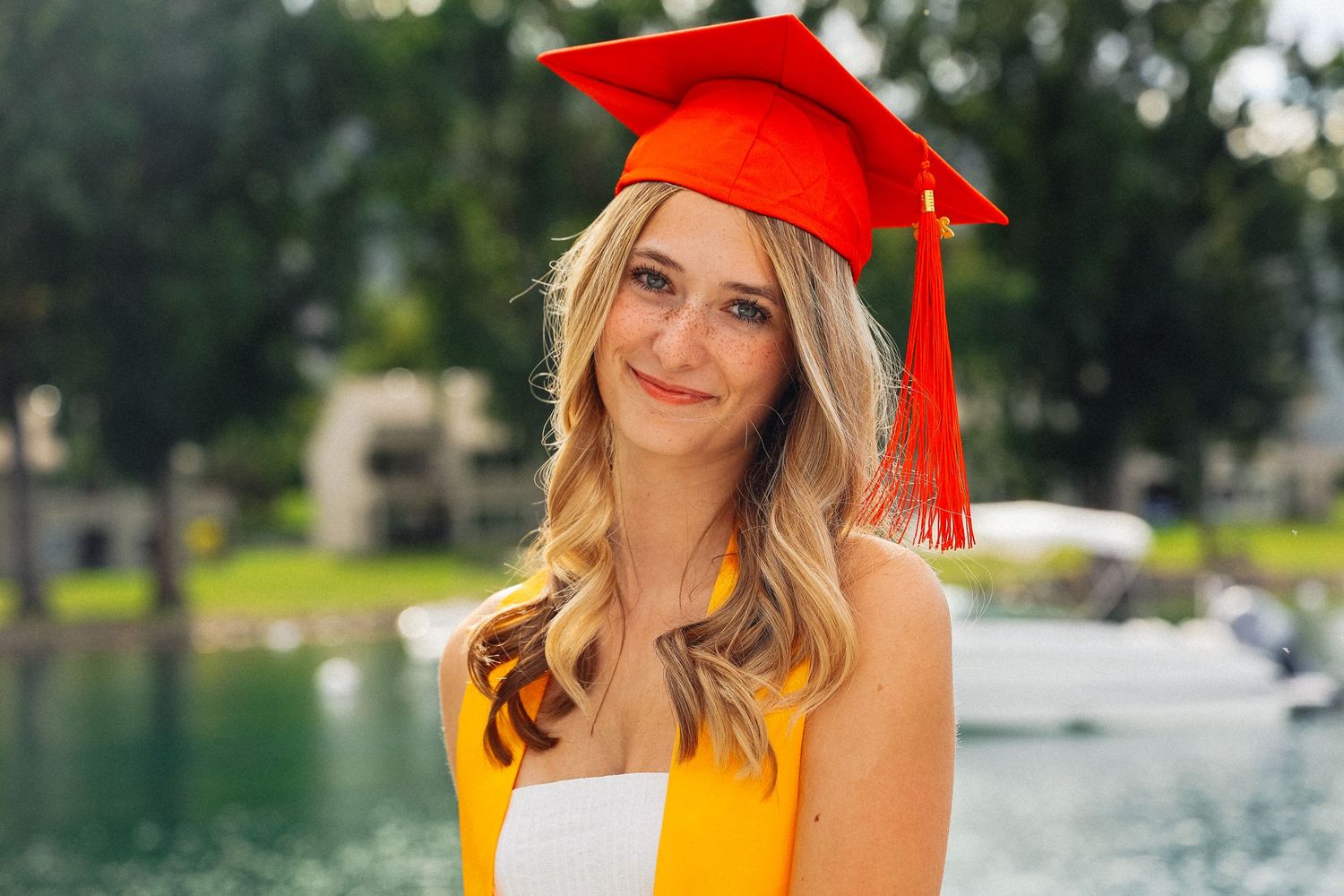 Graduate in orange dress and red cap posing outdoors.