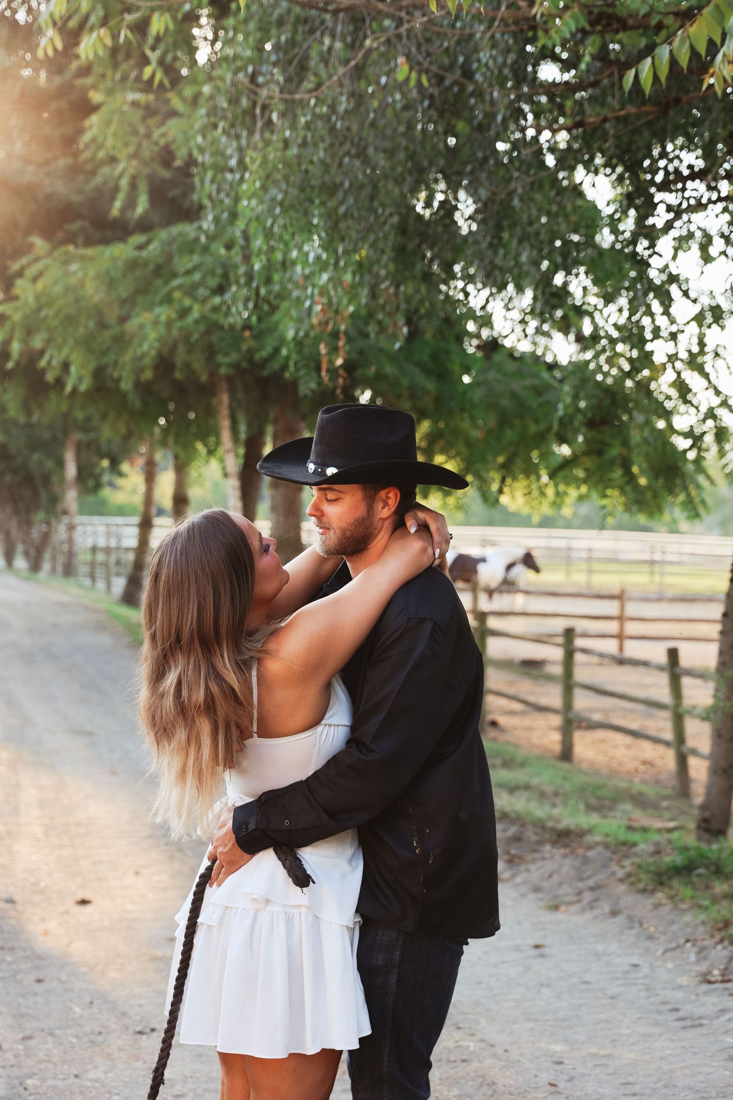 Romantic couple in western attire share intimate moments along a rustic fence.