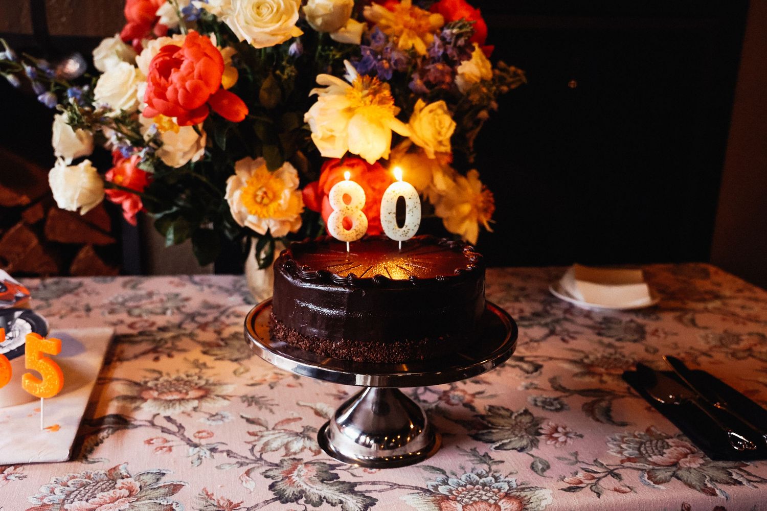 Vibrant floral centerpiece with orange, peach and cream roses on patterned tablecloth.