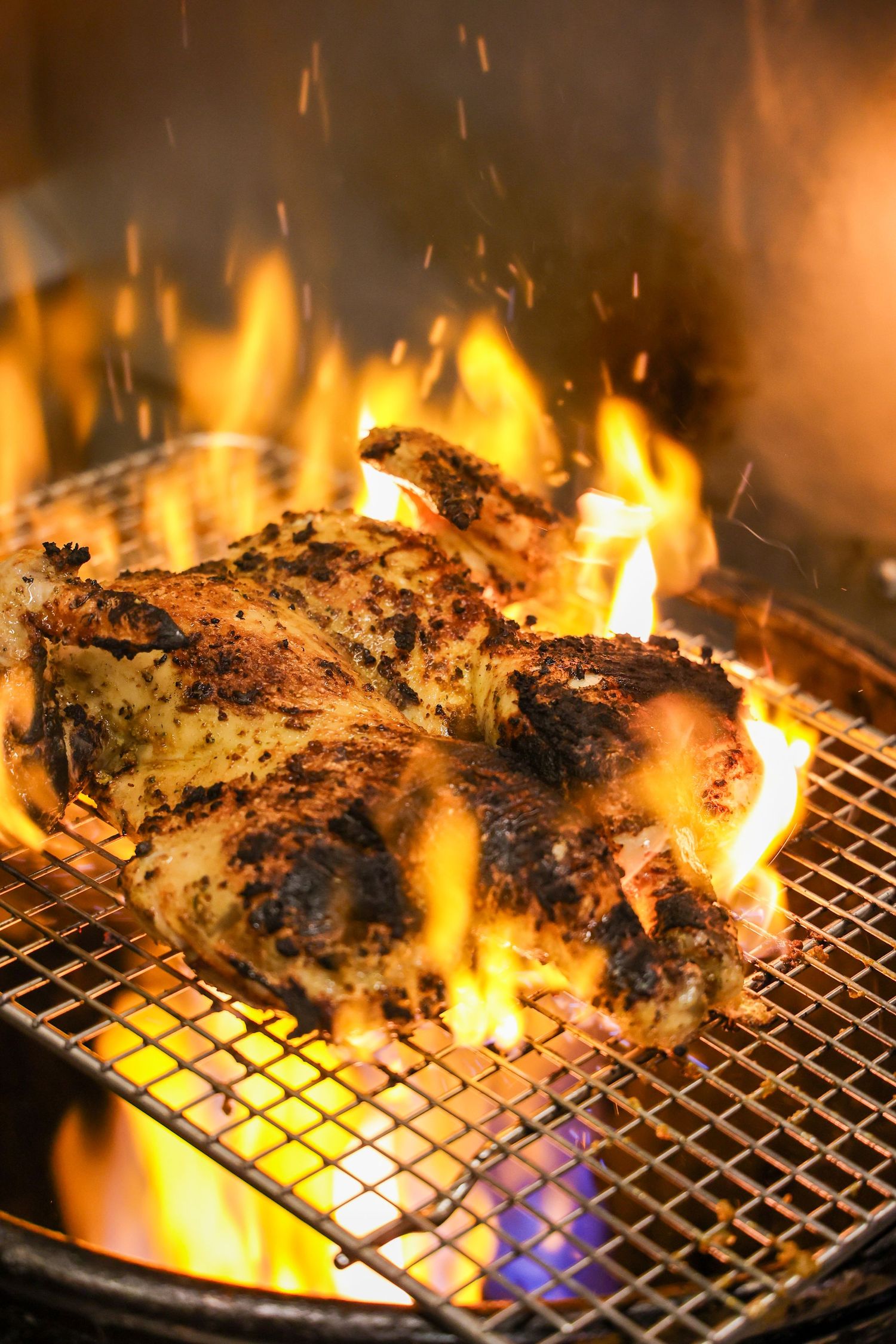 Grilled meat cooking over open flames on a metal grill grate with intense fire.