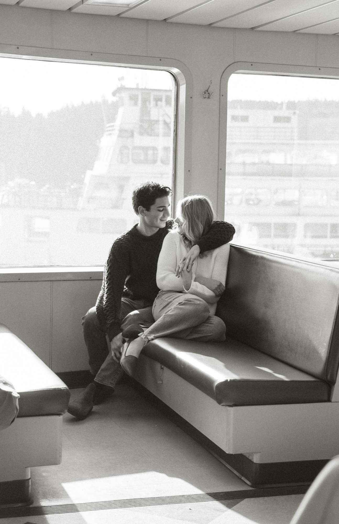 A couple sitting together on benches inside a ferry or boat interior.