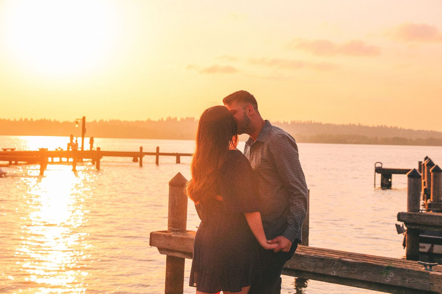 Silhouetted couple sharing romantic moment on dock at sunset with golden light reflecting off calm waters.