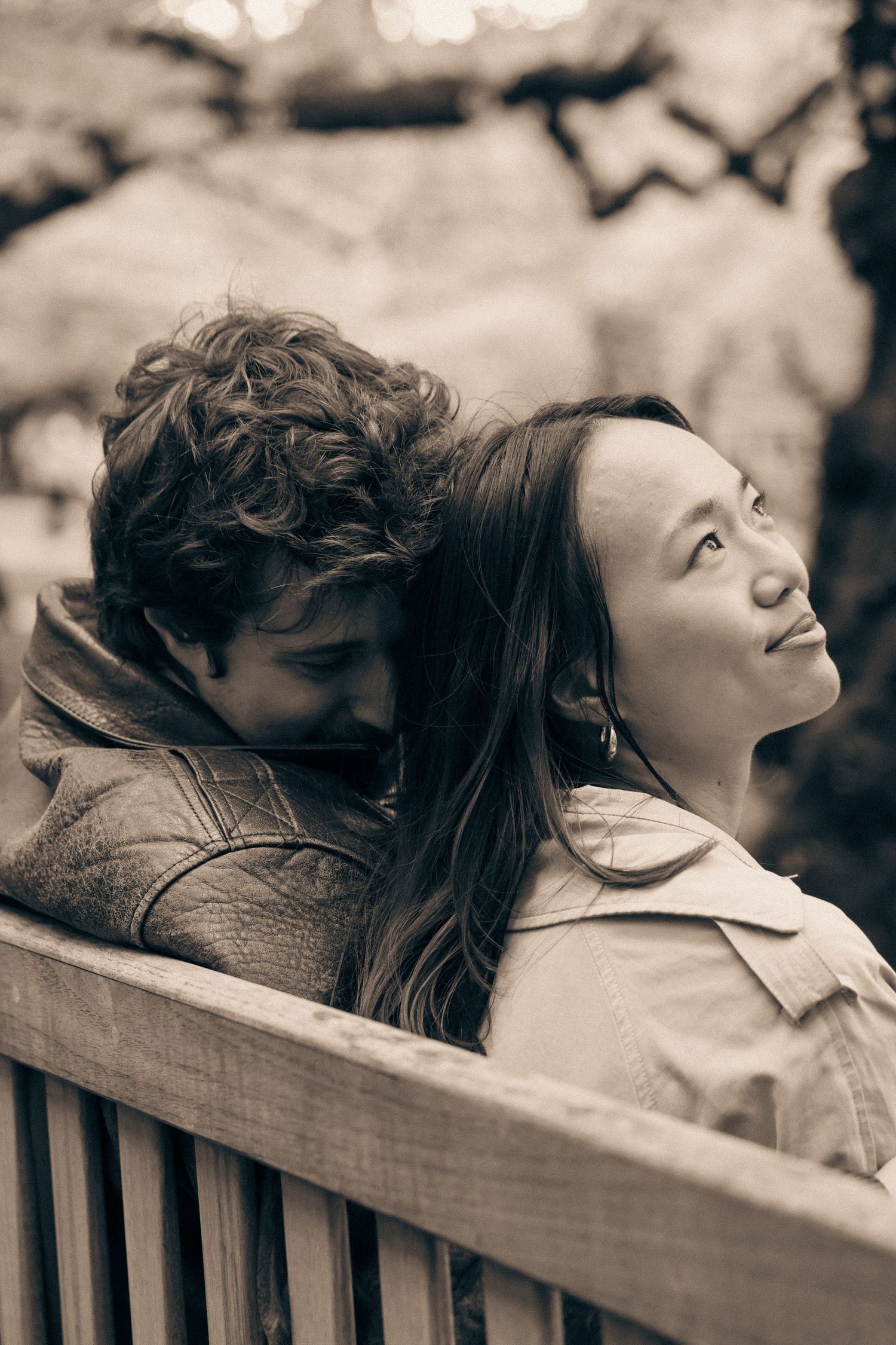 A couple shares an intimate moment sitting together on a wooden bench in a sepia-toned photograph.