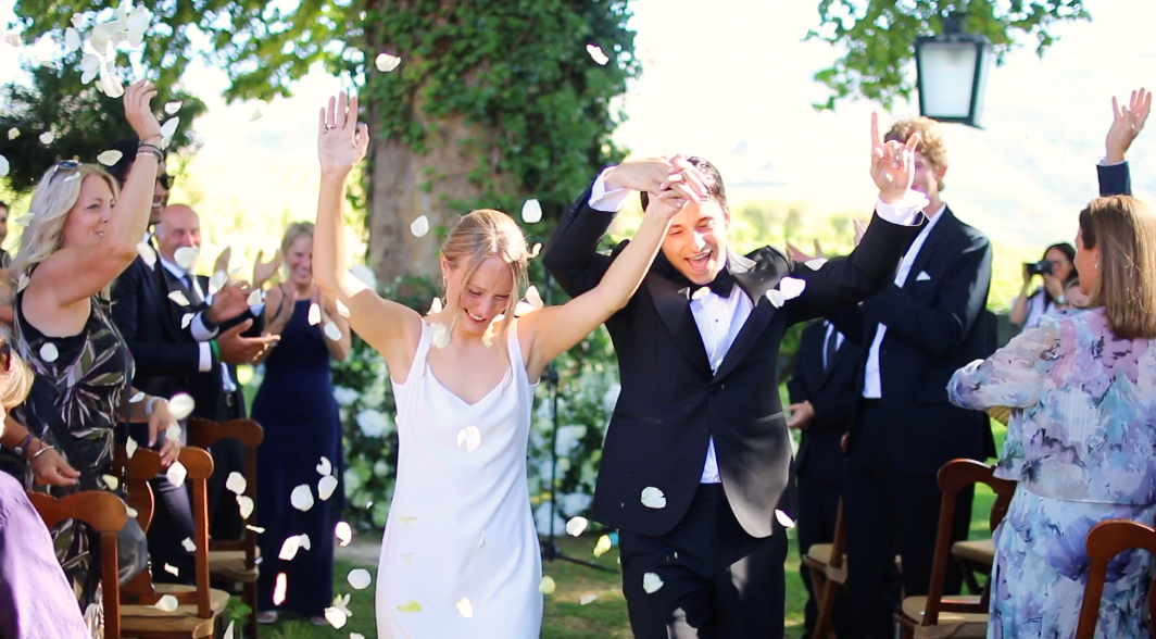Wedding celebration with guests throwing confetti in an outdoor garden setting.