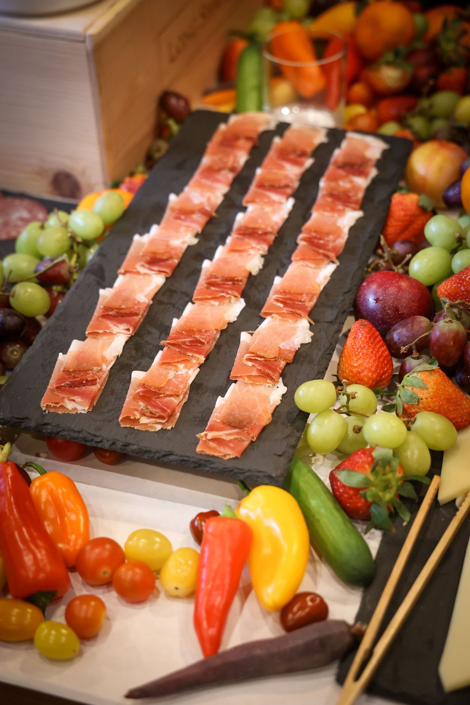 Fresh fruit platter with colorful berries, grapes, and sliced raw salmon arranged on black slate boards for catering.
