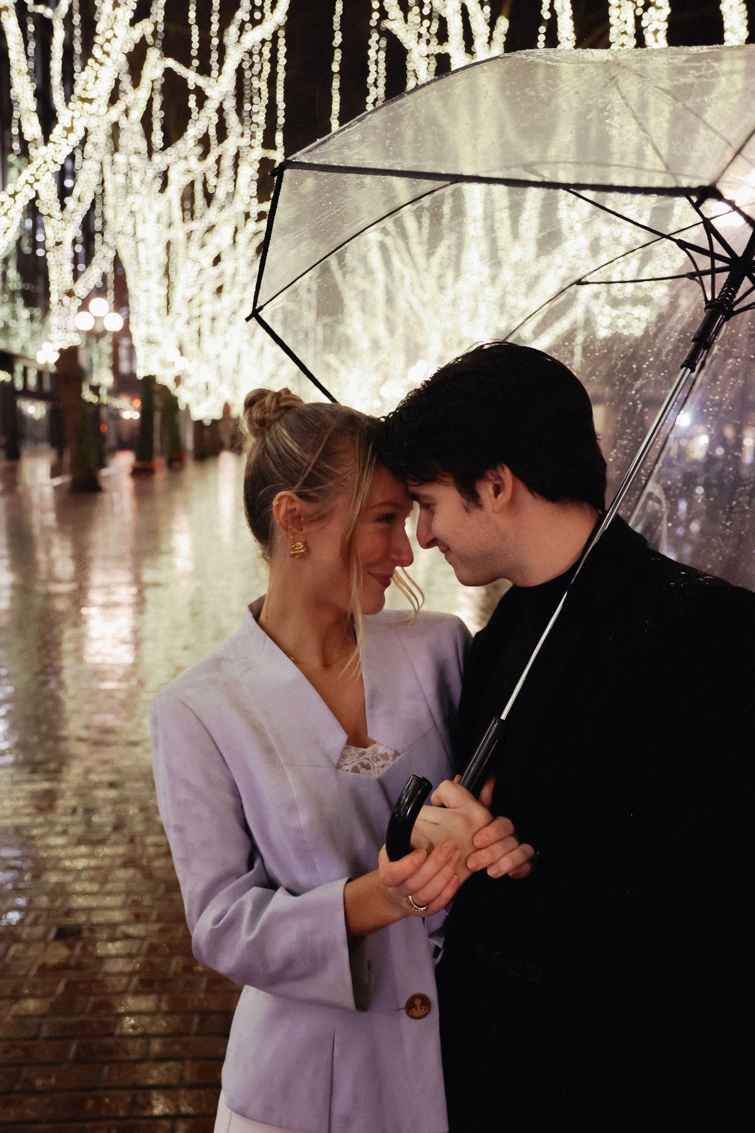 A couple shares an intimate moment under an umbrella with twinkling lights in background.