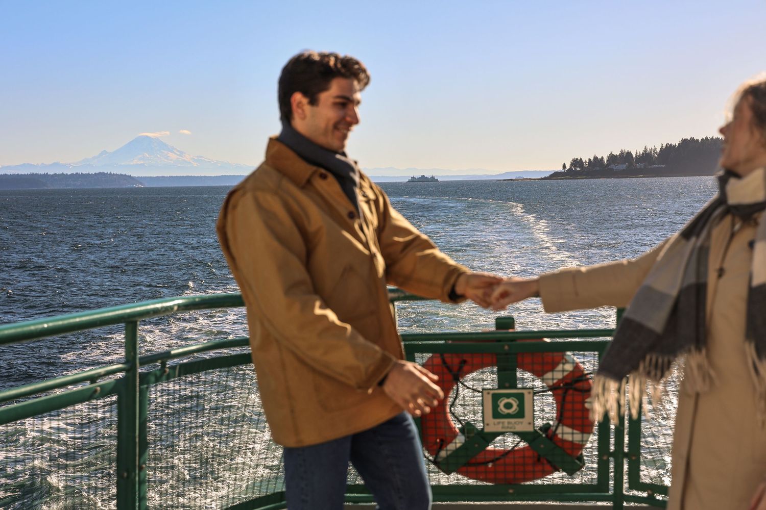 A couple stands on a deck overlooking a scenic coastal view while exchanging wedding rings during an outdoor ceremony.