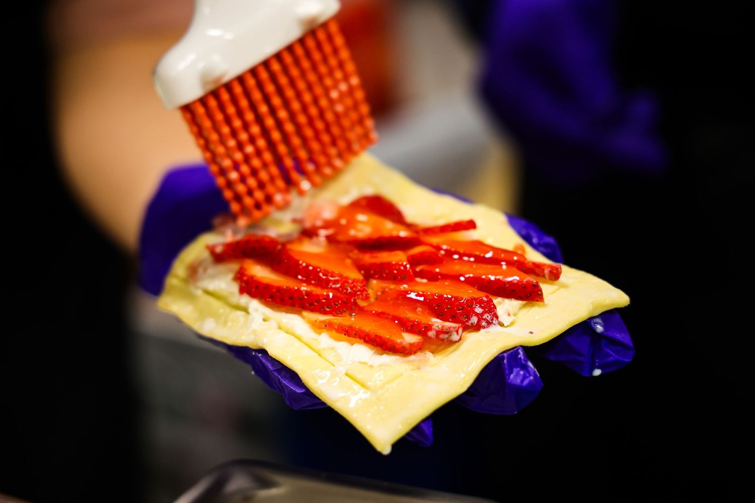 Close-up of sliced meat being placed on yellow cheese against dark background.