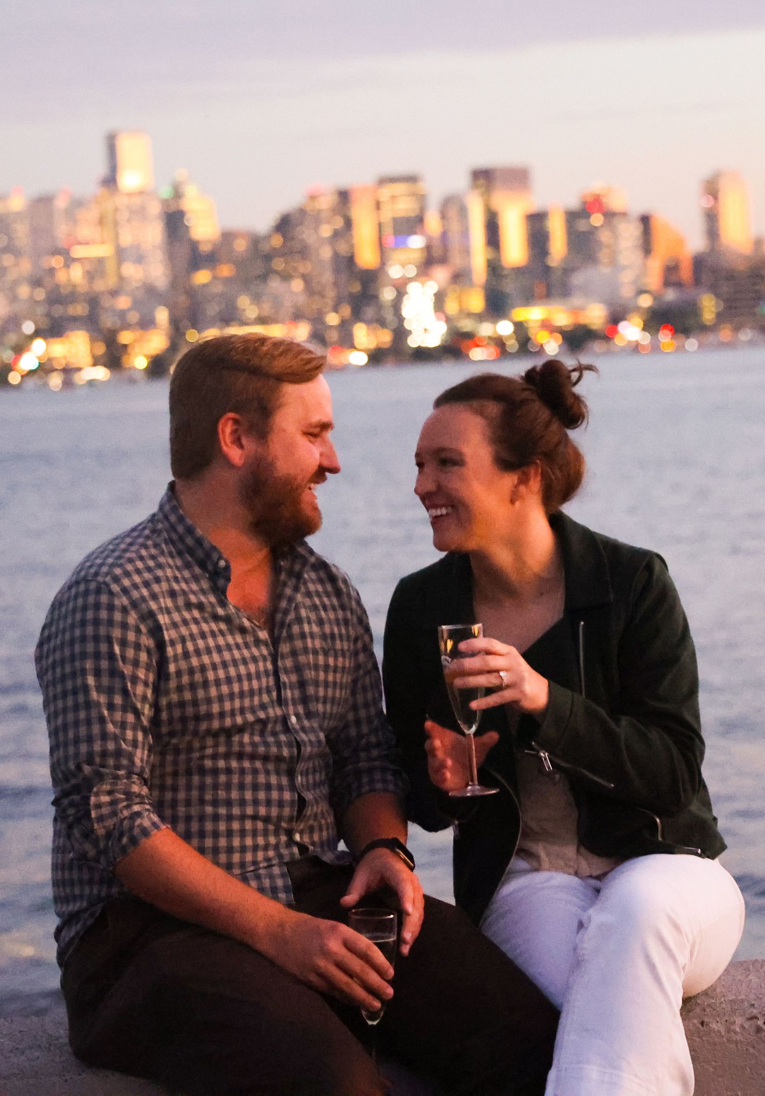 Couple enjoying drinks at sunset with city skyline in background.