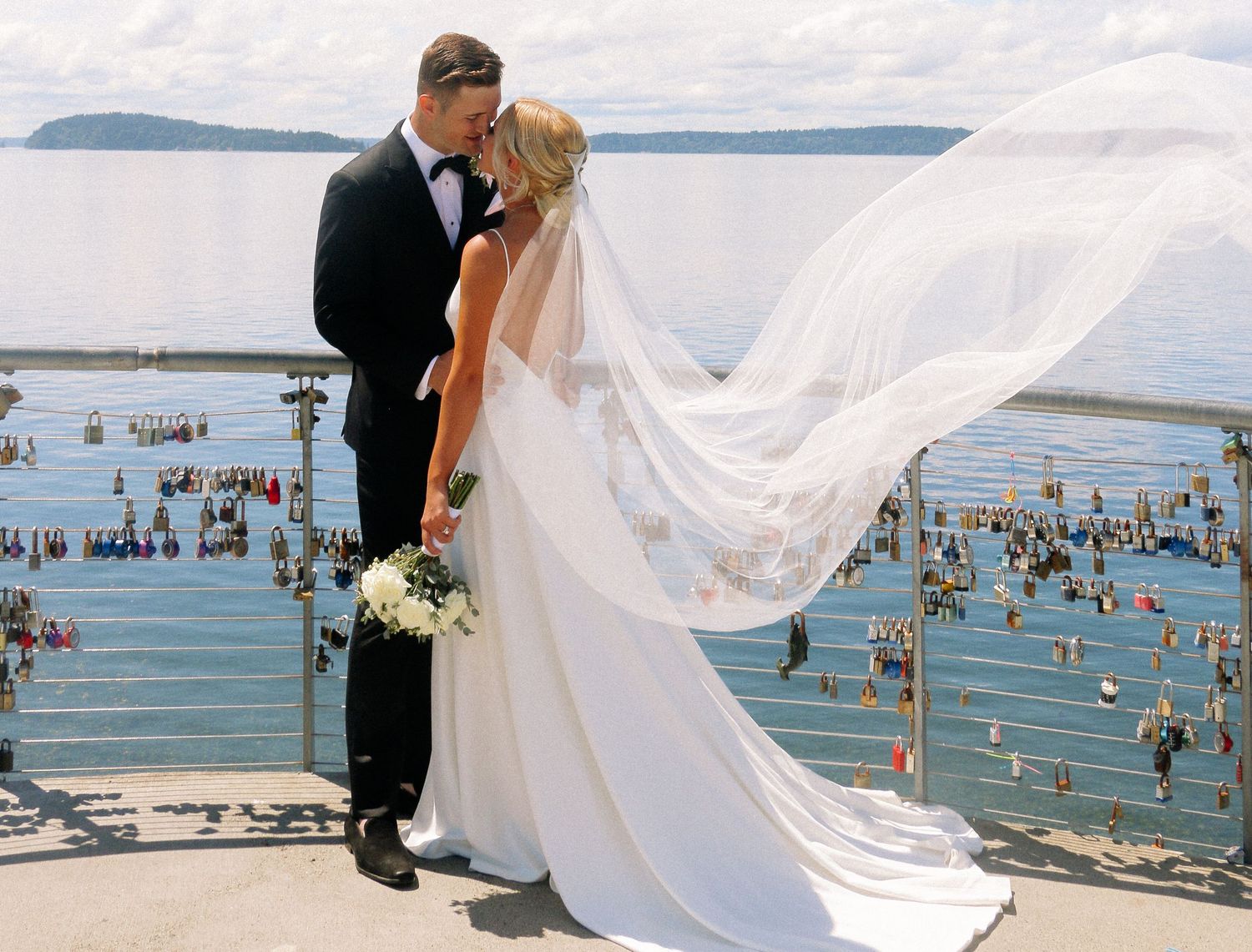 Wedding ceremony on waterfront deck with flowing white veil and ocean backdrop.