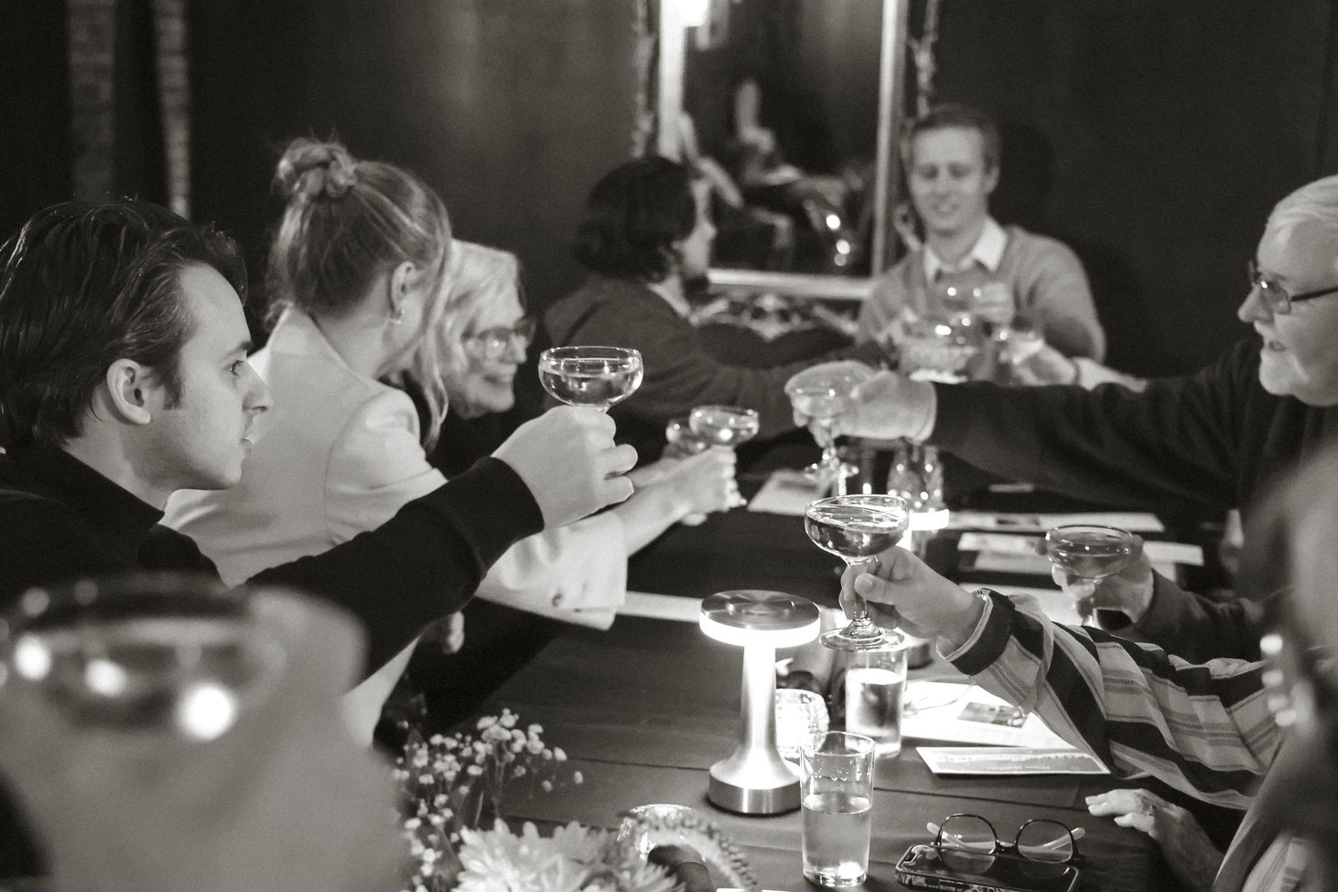 Black and white photo of people dining together at a candlelit table in a restaurant.