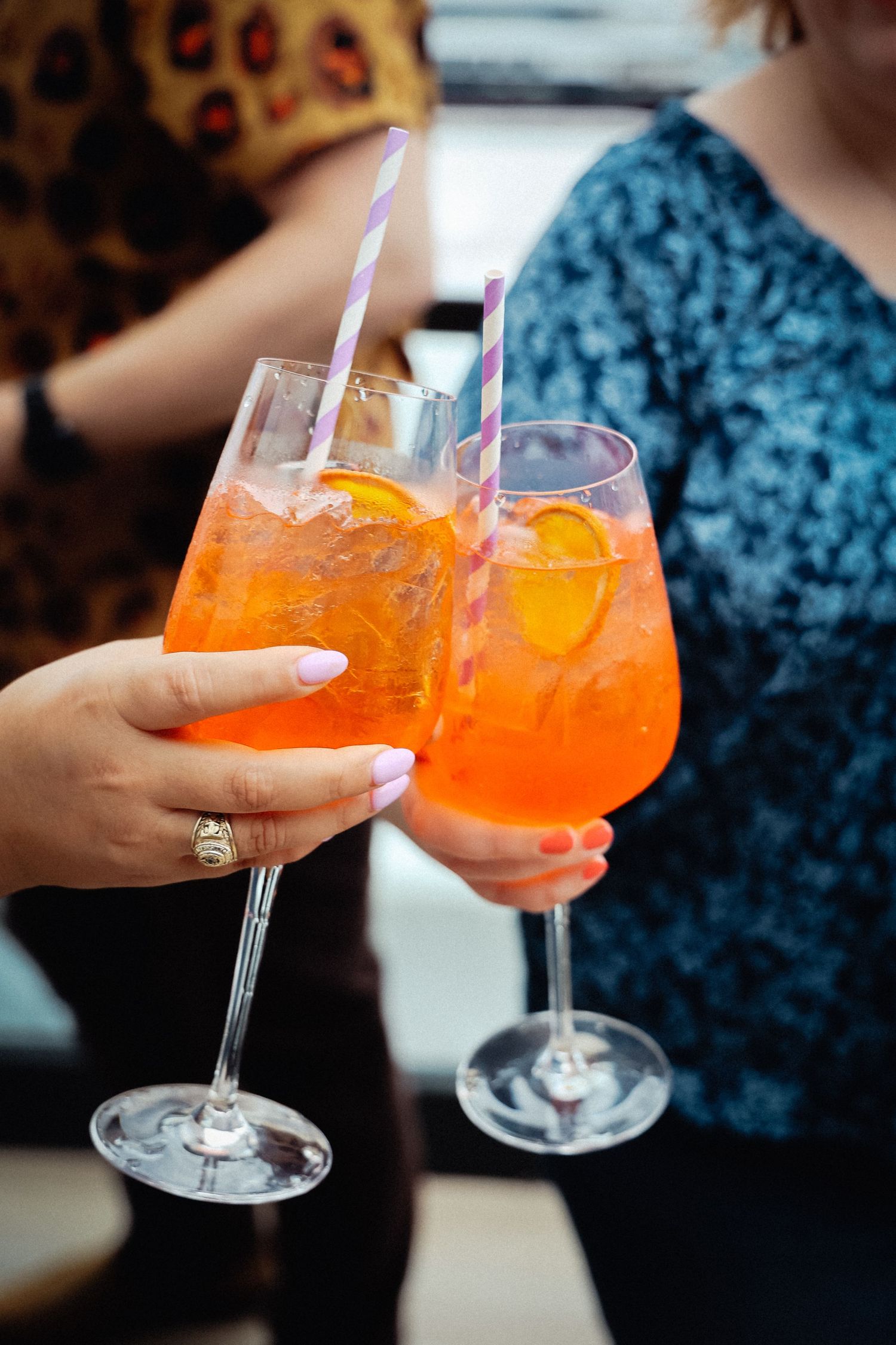 Orange cocktails with straws in stemmed glasses being toasted against dark background.