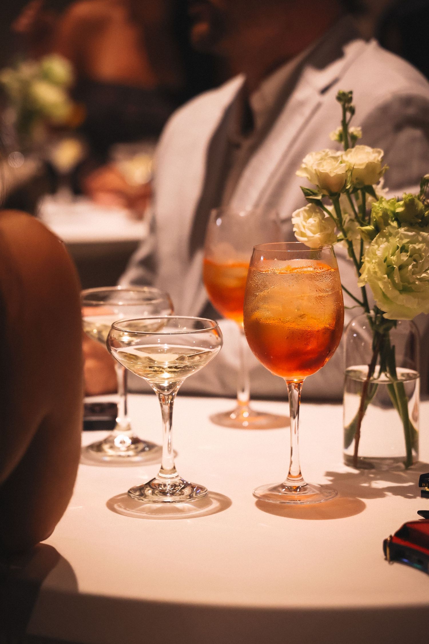 Elegant cocktails and flowers on white tablecloth at upscale restaurant.