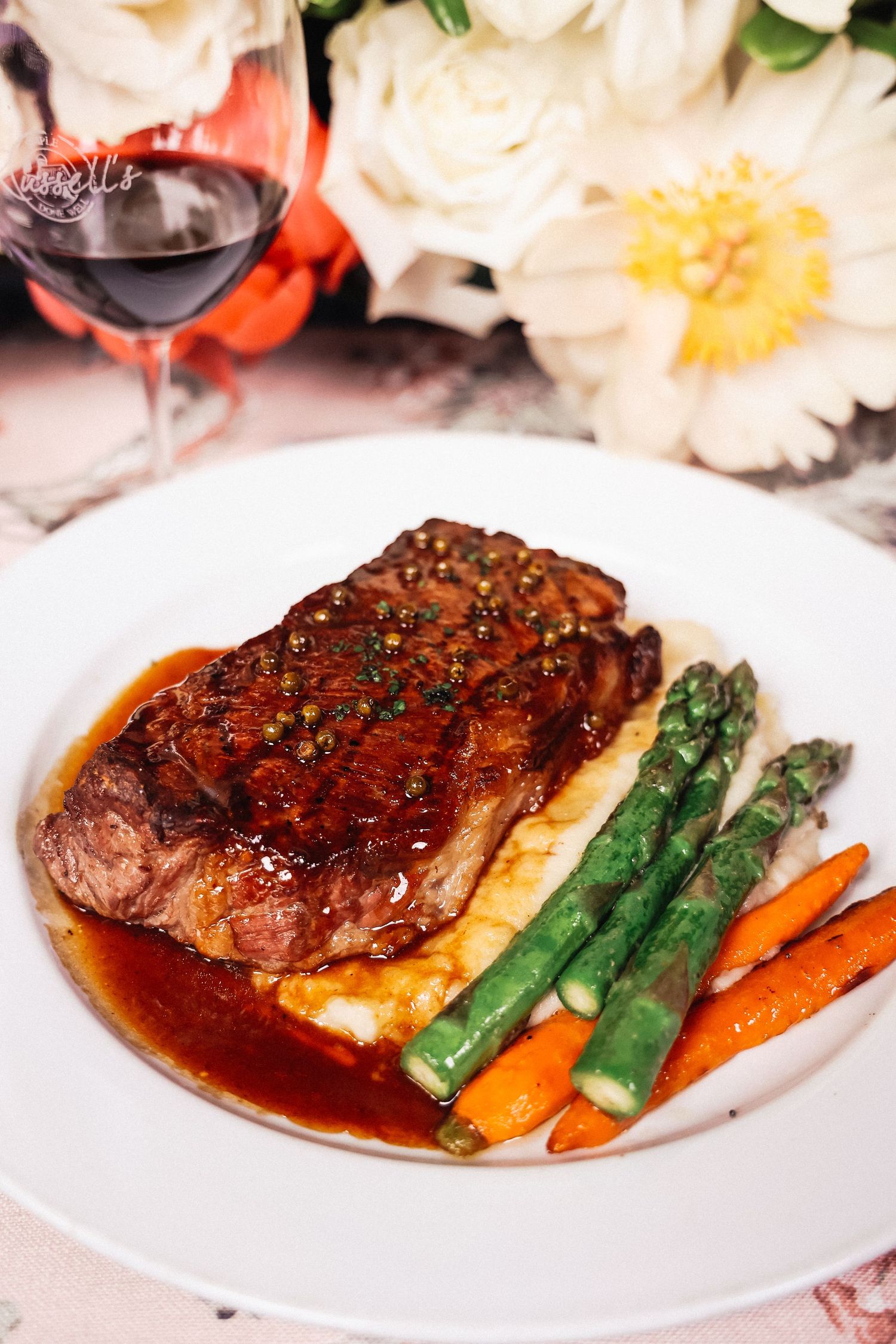 Grilled steak dinner with asparagus and carrots in rich sauce on white plate.