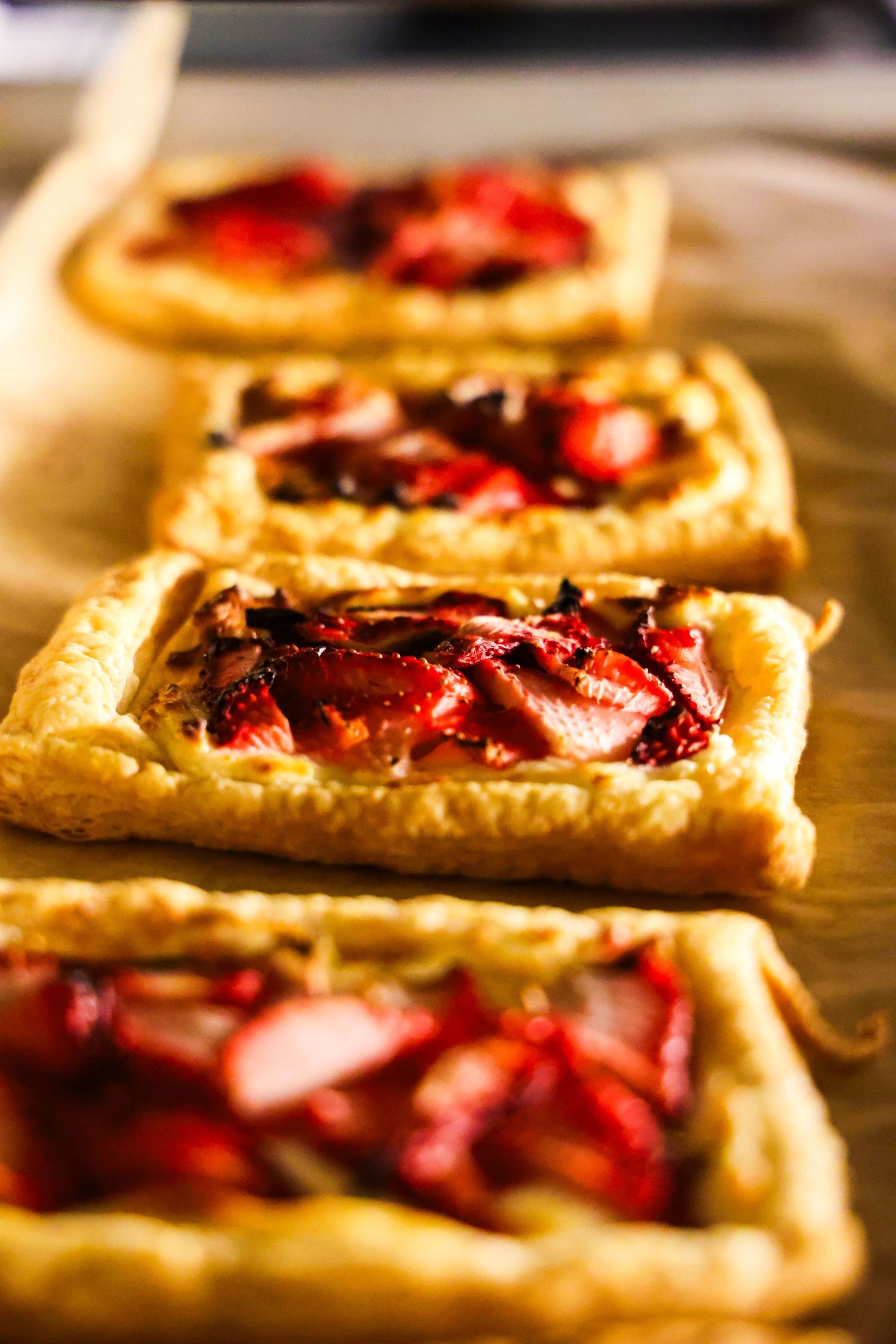 Homemade pastries with strawberry filling on golden puff pastry displayed on wooden surface.