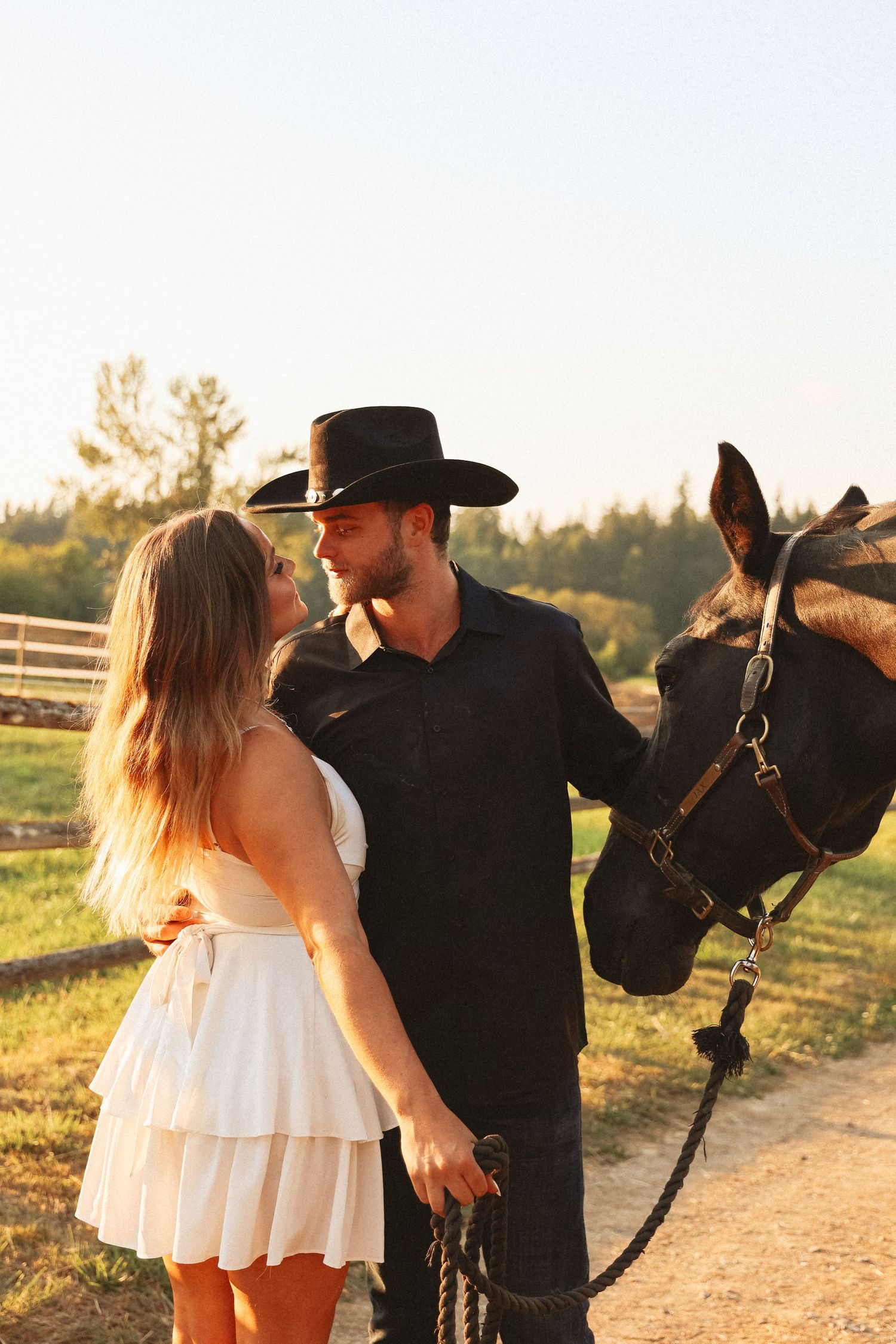 Romantic couple poses with horse at sunset in rustic countryside setting.