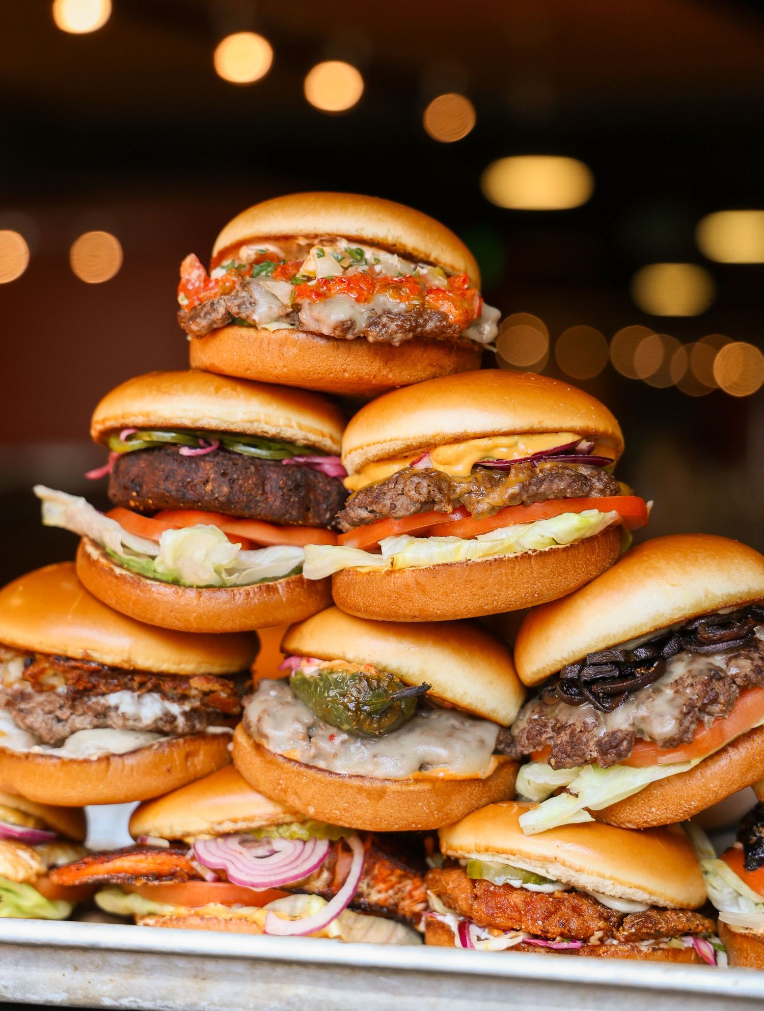 Row of juicy hamburgers lined up on display with various toppings and condiments.