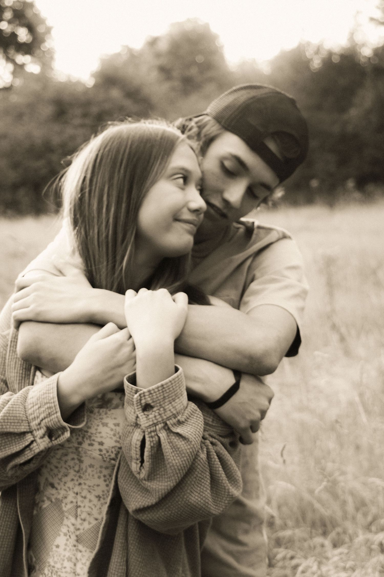 A romantic sepia-toned portrait of a couple embracing in a field, with soft natural lighting and dreamy atmosphere.