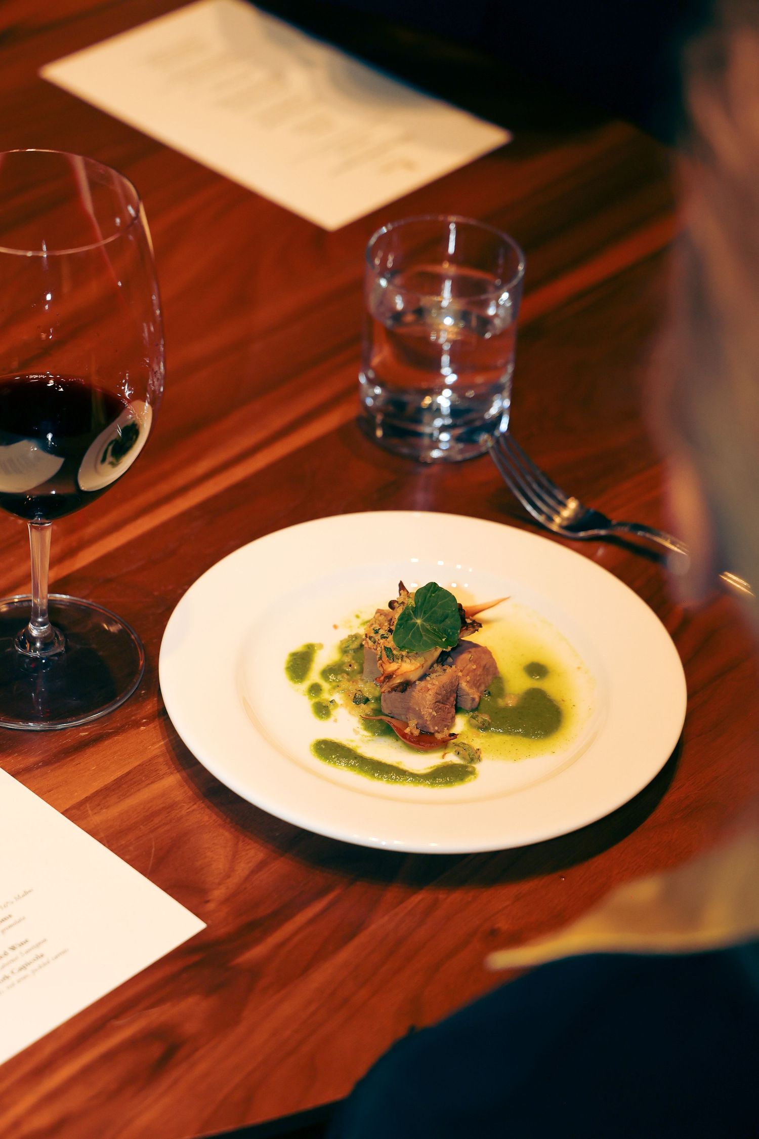 Wine glasses and elegant plated dishes on a dark wooden table in an upscale restaurant setting.