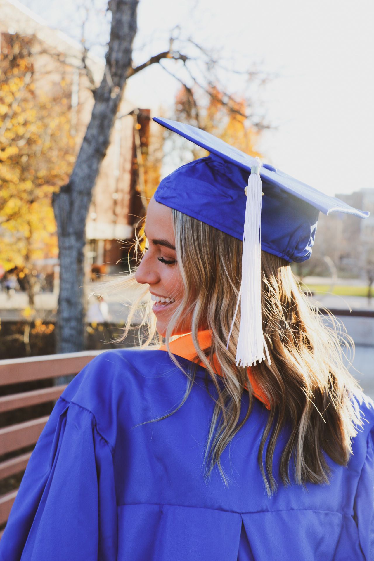 Graduate in blue cap and gown smiling during outdoor photo session in autumn.
