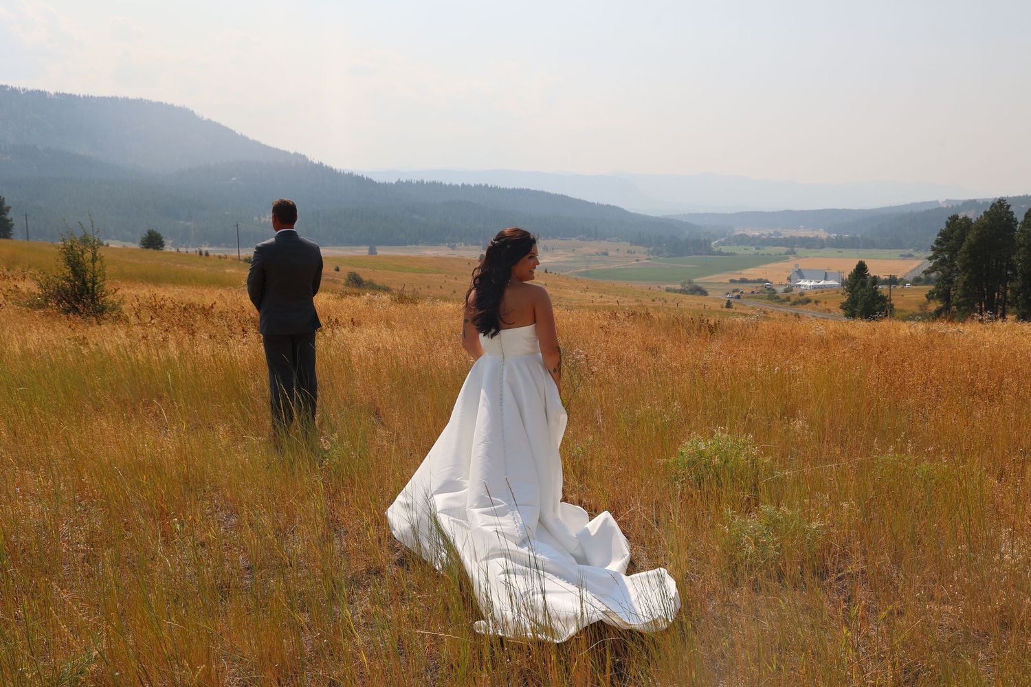 Wedding couple walking through golden grass field with mountains in background.
