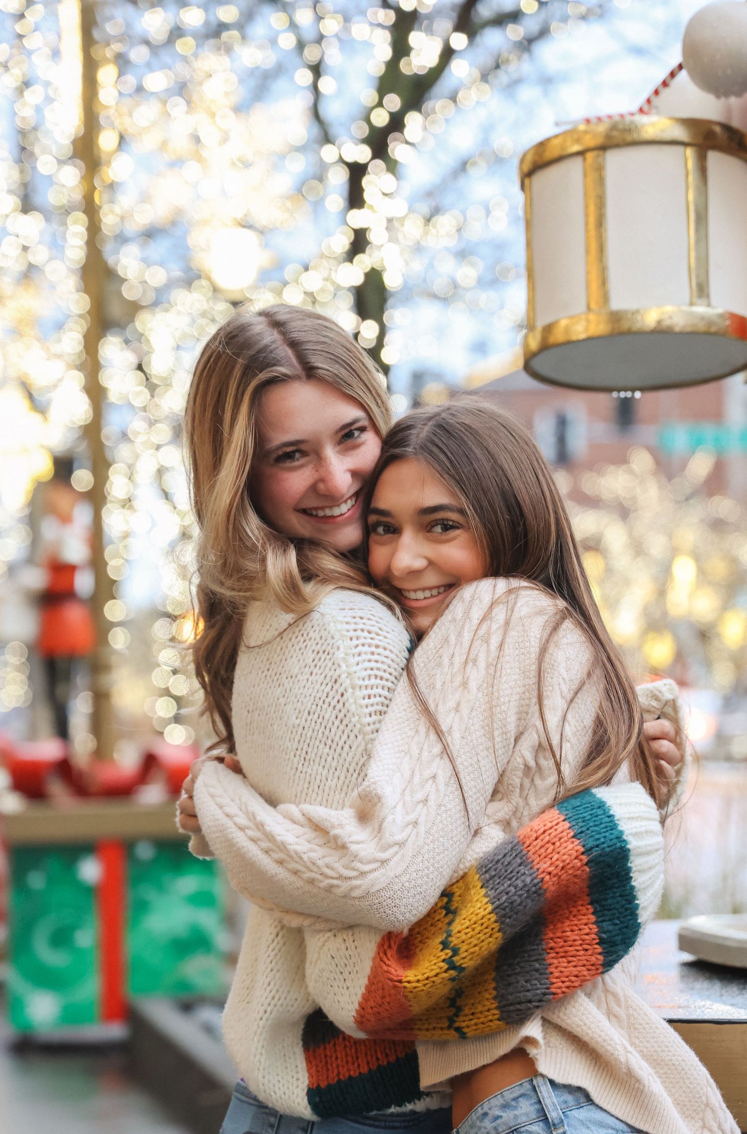 Friends embracing in cozy winter sweaters against festive holiday lights.