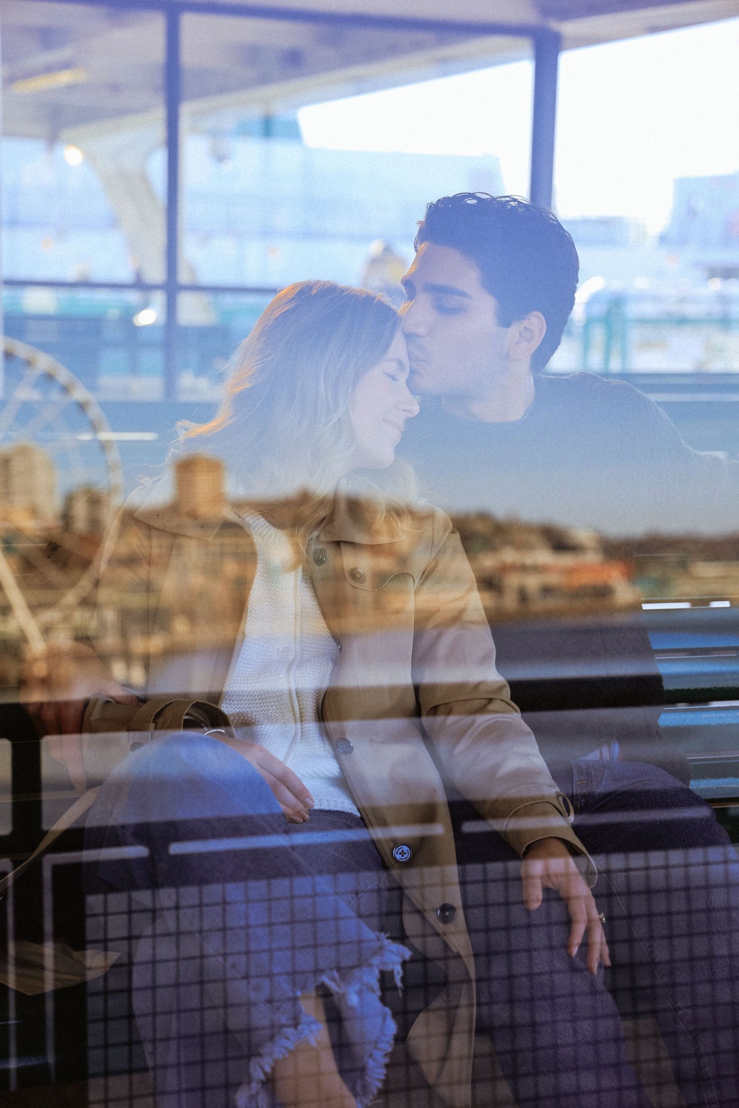A couple shares an intimate moment by a window with city views.