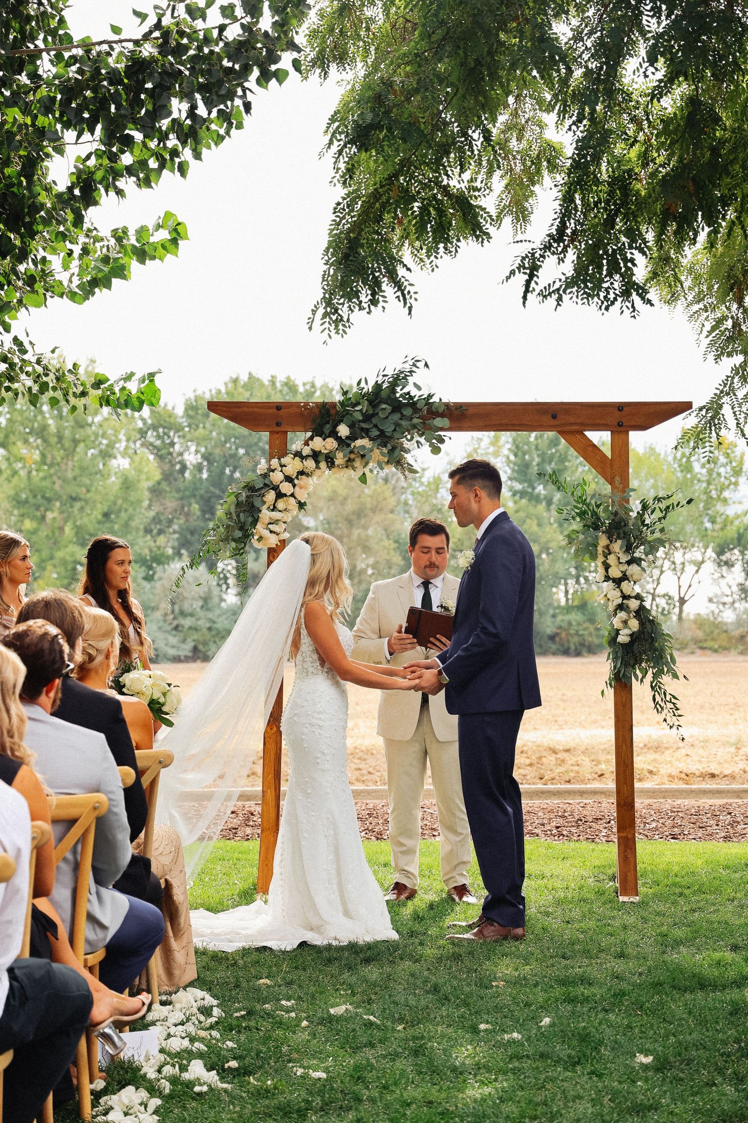 Outdoor wedding ceremony under wooden arbor with greenery and natural landscape.