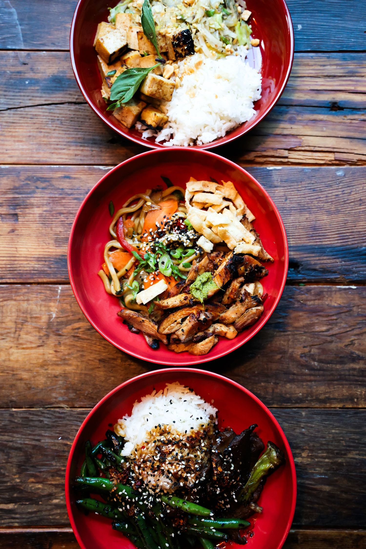 Asian-inspired rice bowls with vegetables and proteins served in red ceramic bowls.