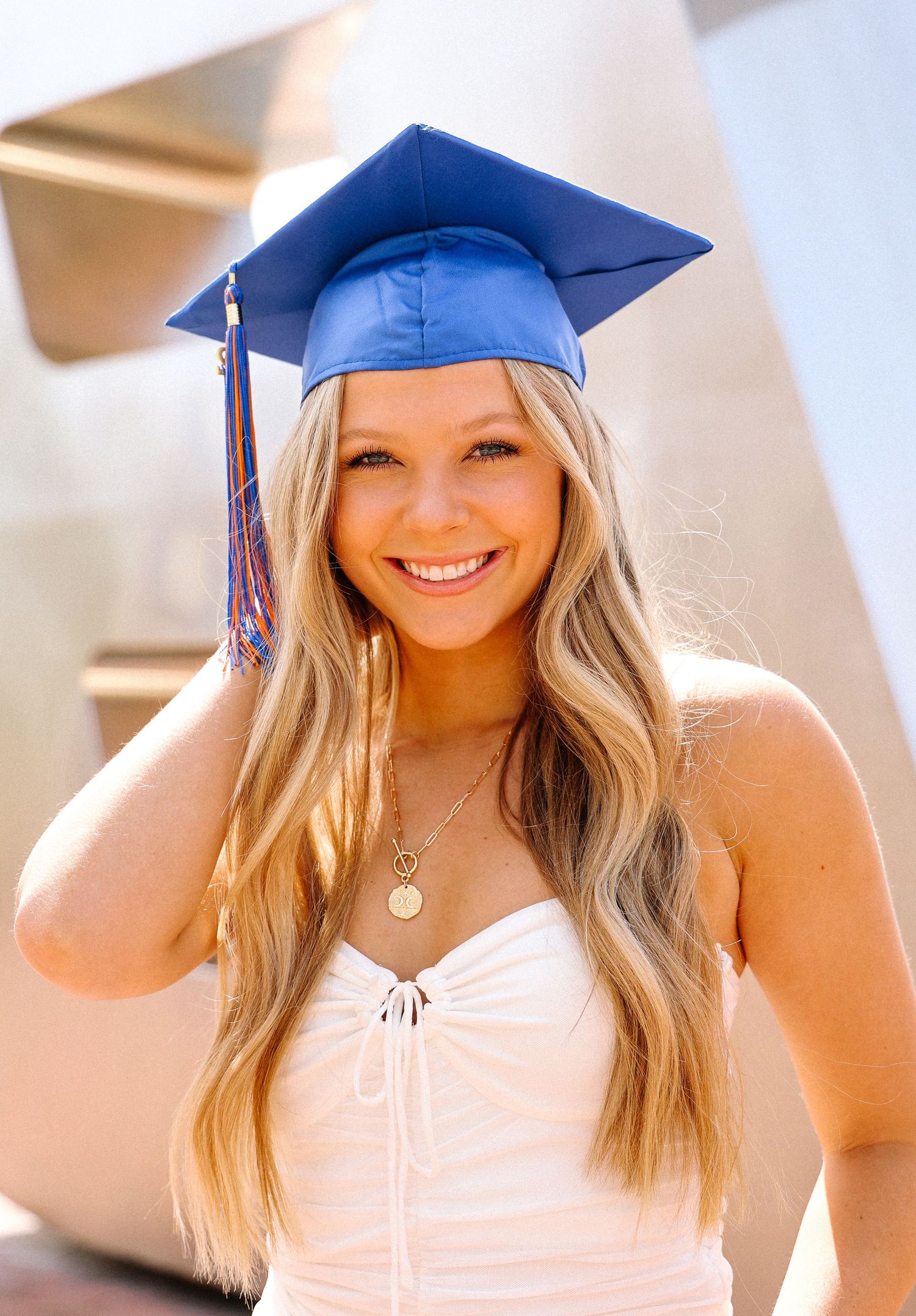 Graduate in blue cap and white dress smiles during graduation photoshoot.