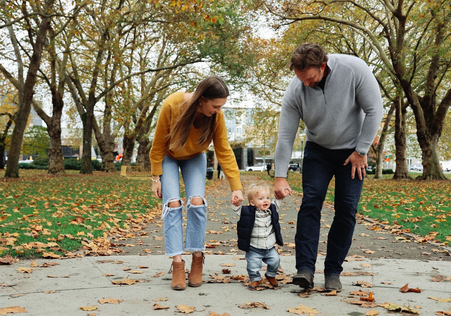 Candid family moments captured on fallen leaves in autumn park setting.