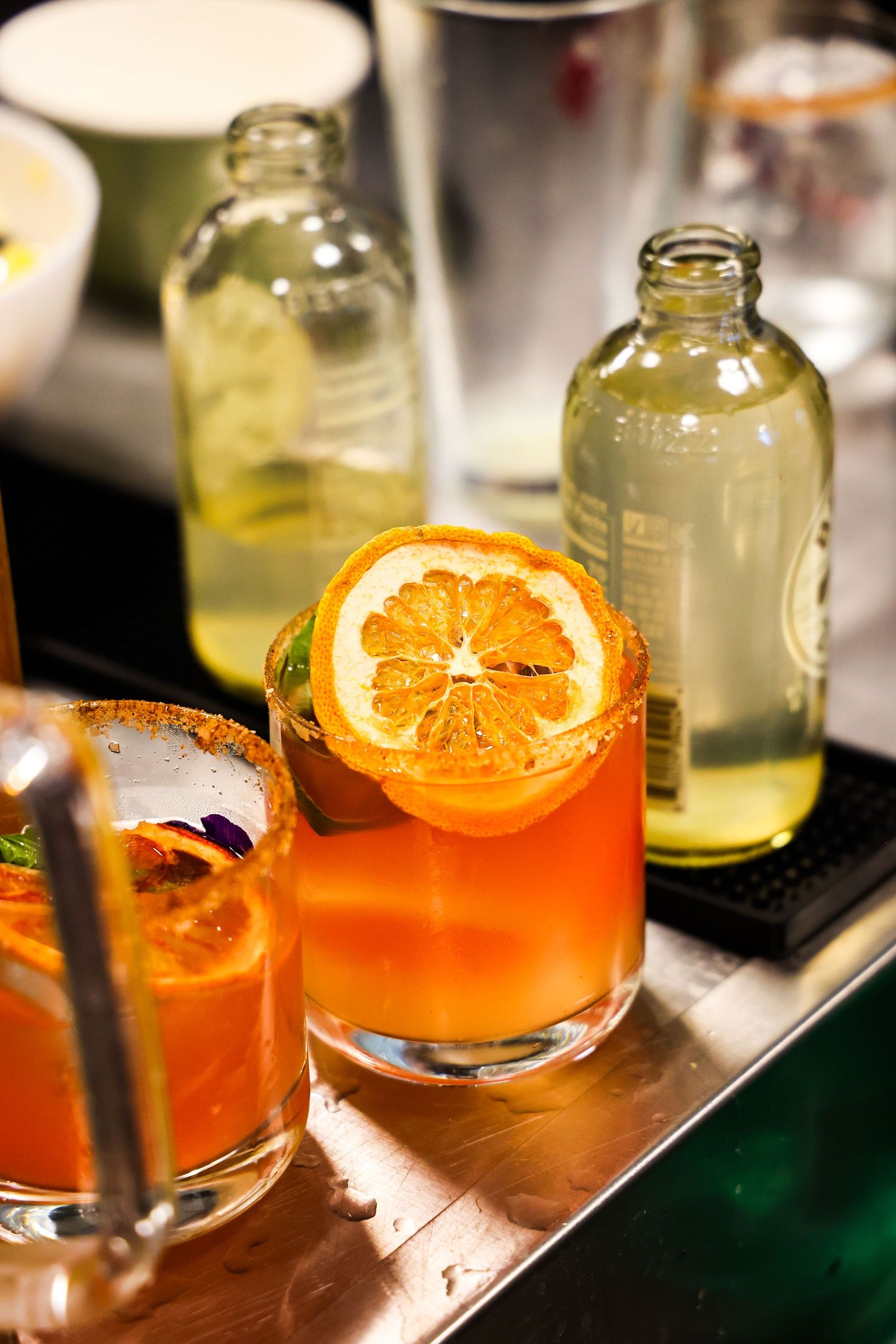 Orange cocktails garnished with citrus slices served in elegant glasses at bar.