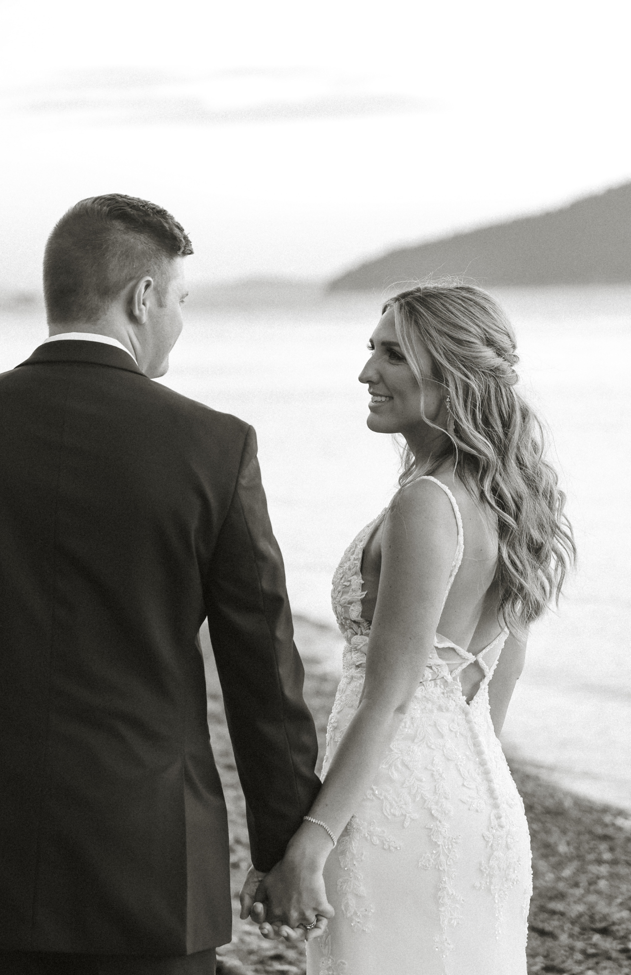 A bride and groom walking together on a beach in black and white.