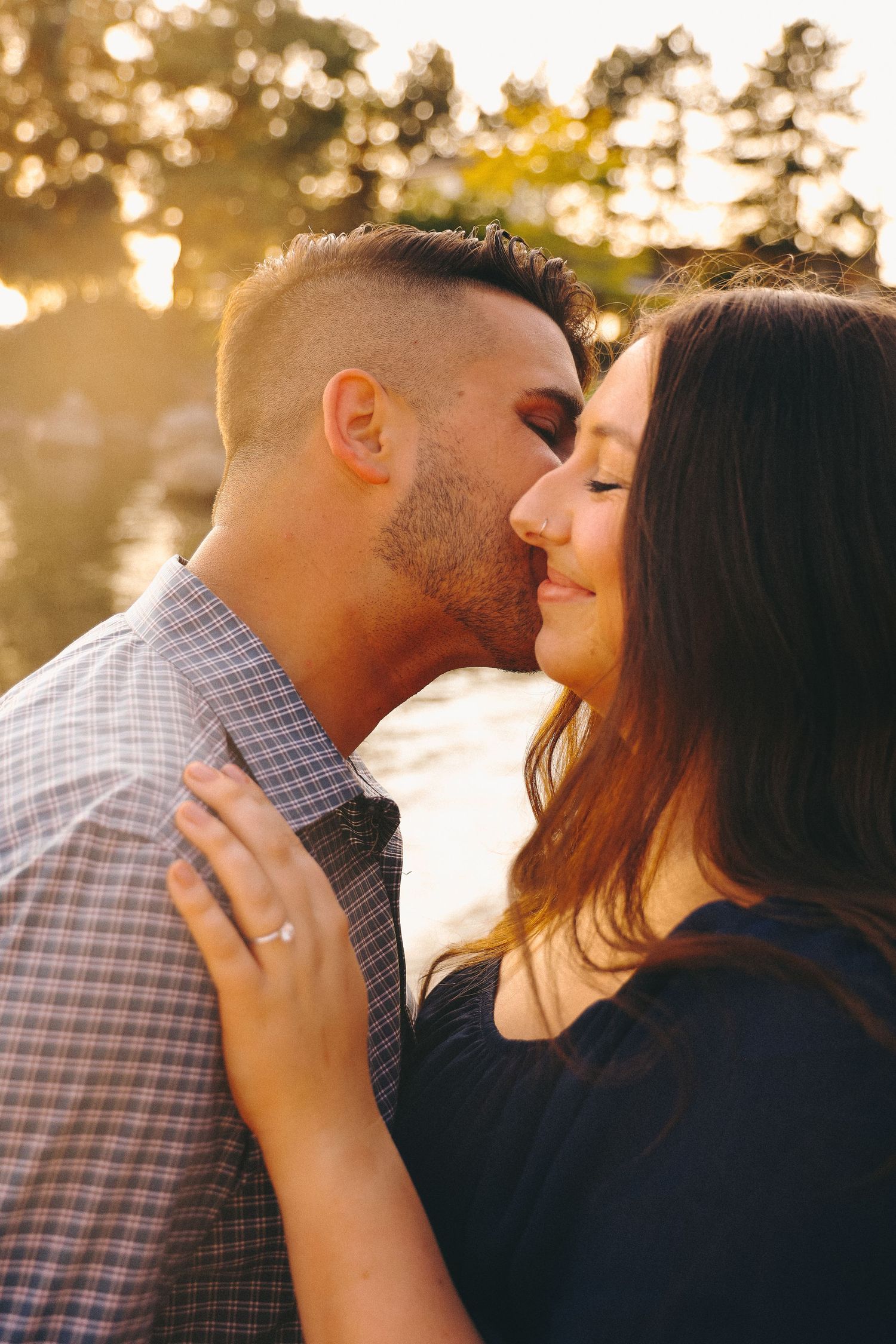 A romantic couple shares tender moments at sunset with golden light filtering through trees in the background.